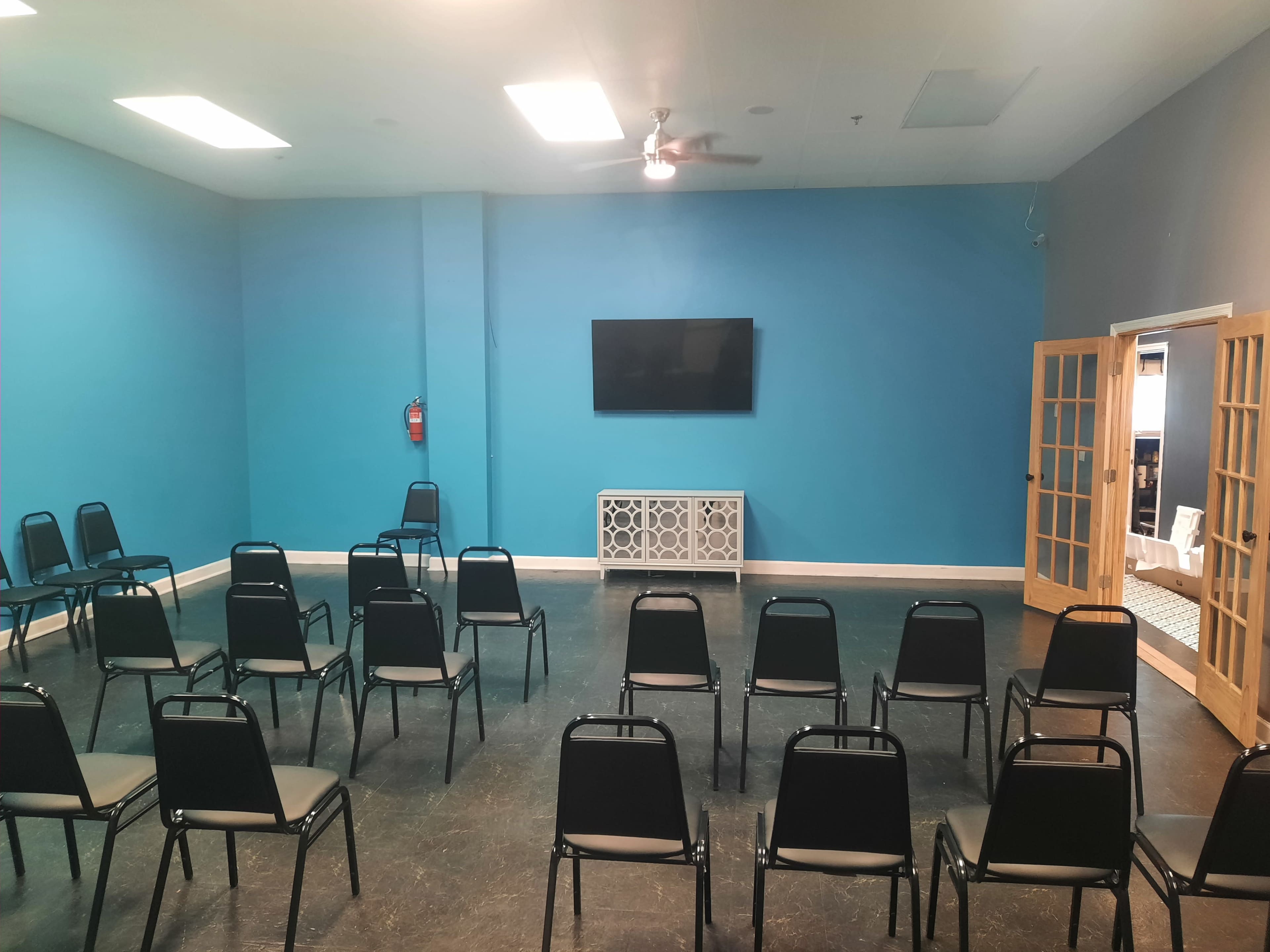 A brightly colored room contains rows of black chairs facing a mounted television on a turquoise wall.