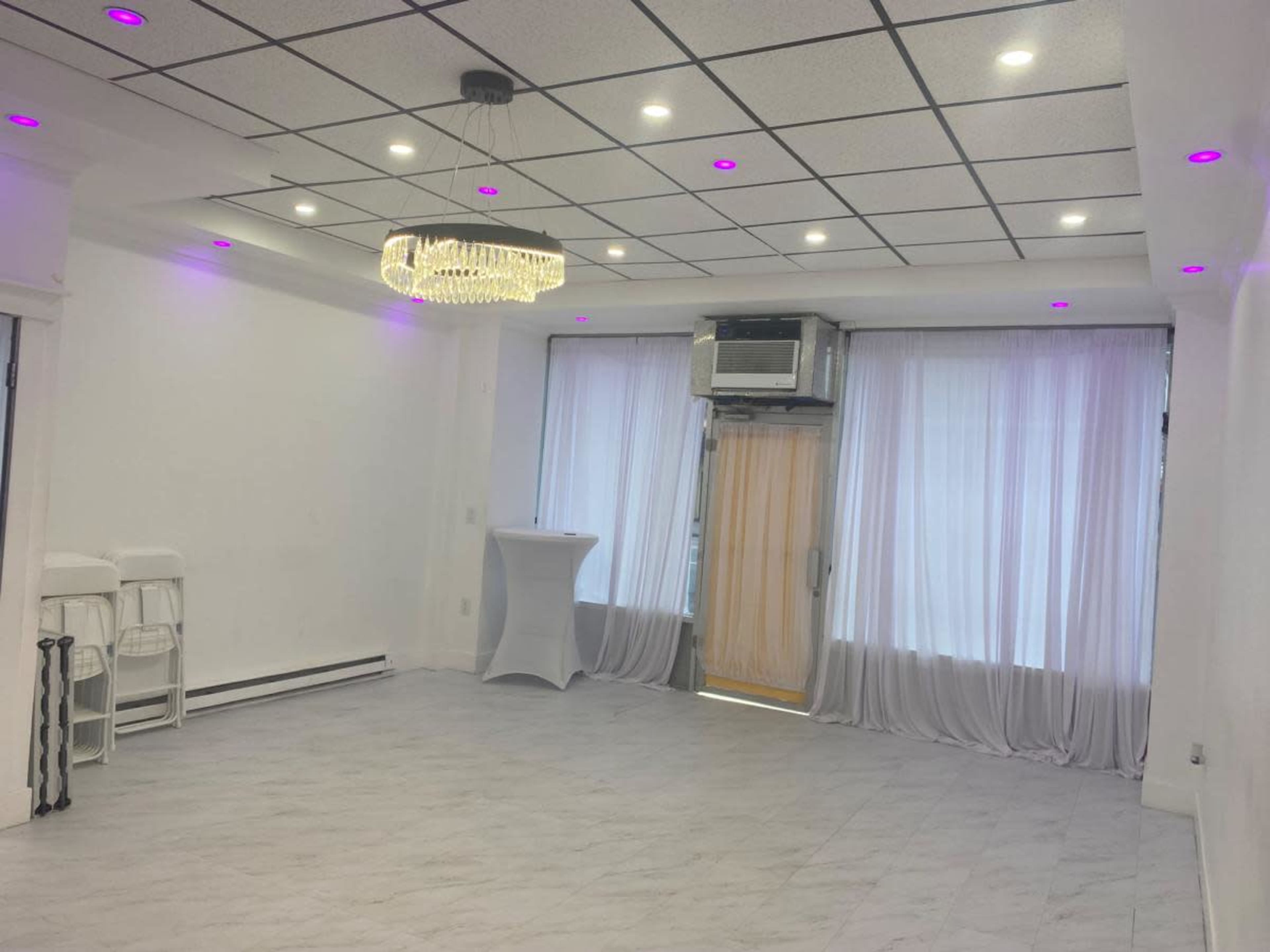 The image shows an empty room with white walls, a light-colored floor, a chandelier, and pink LED lights along the ceiling.