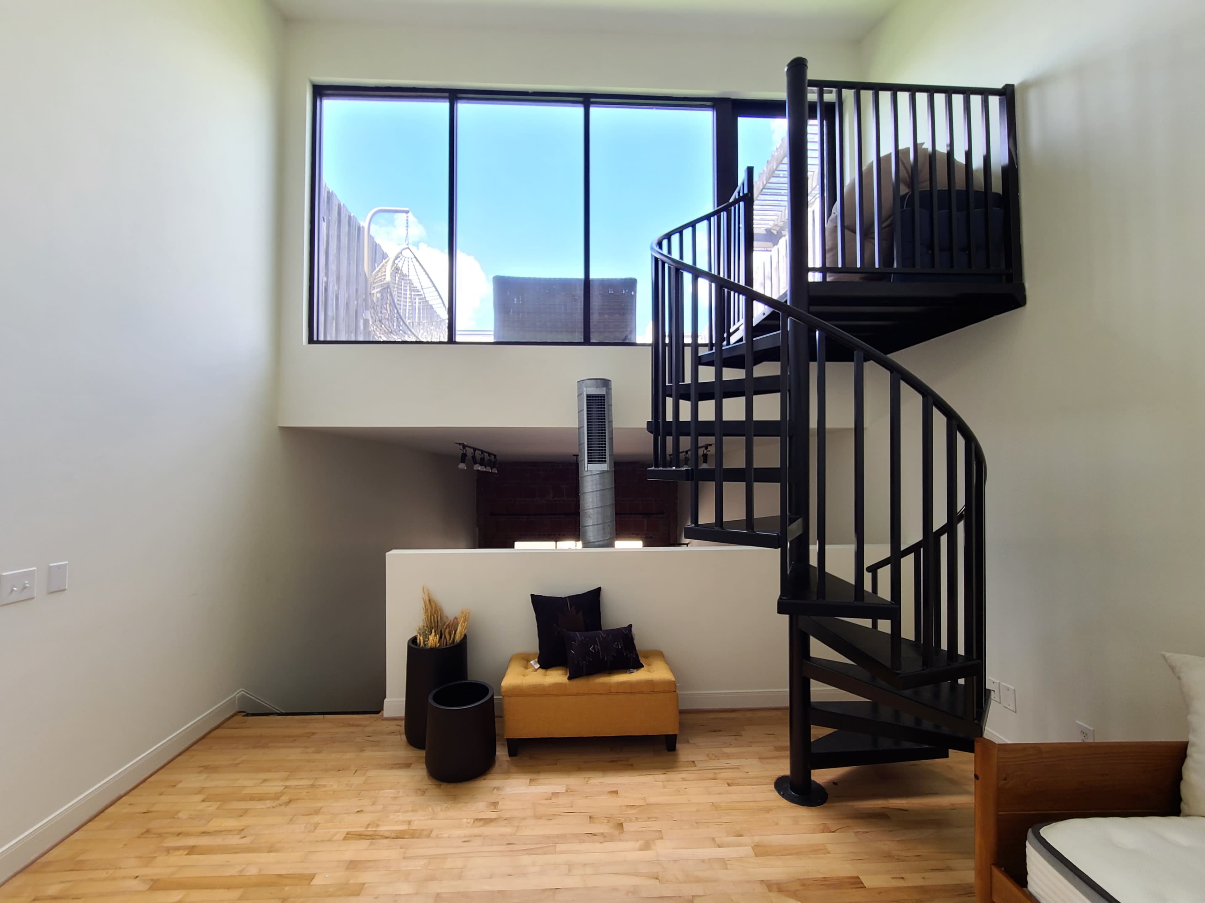 A modern room with a spiral staircase leading to an upper level, featuring large windows and minimalist furnishings.