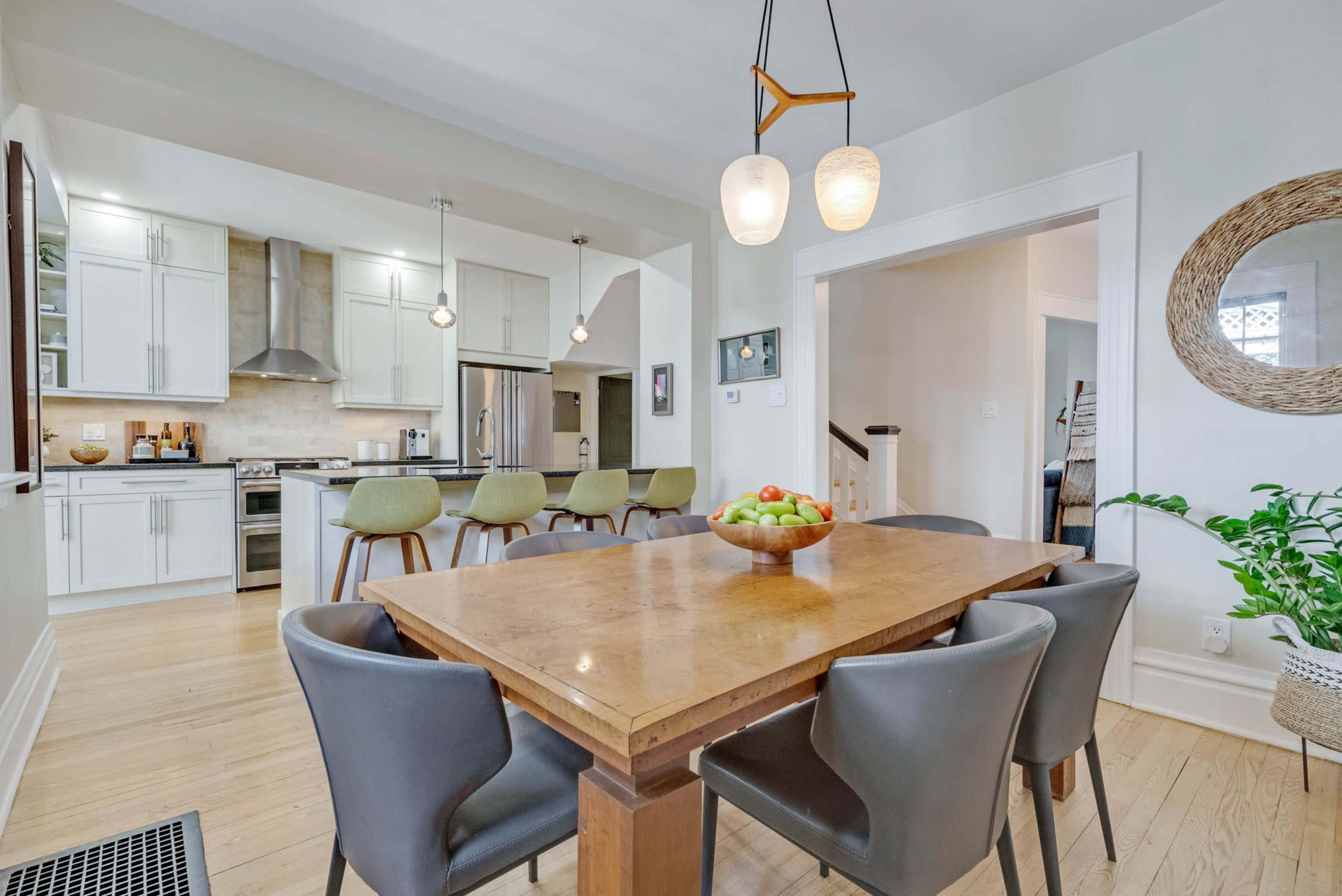 A modern kitchen and dining area featuring a wooden table with gray chairs, pendant lighting, and stainless steel appliances.