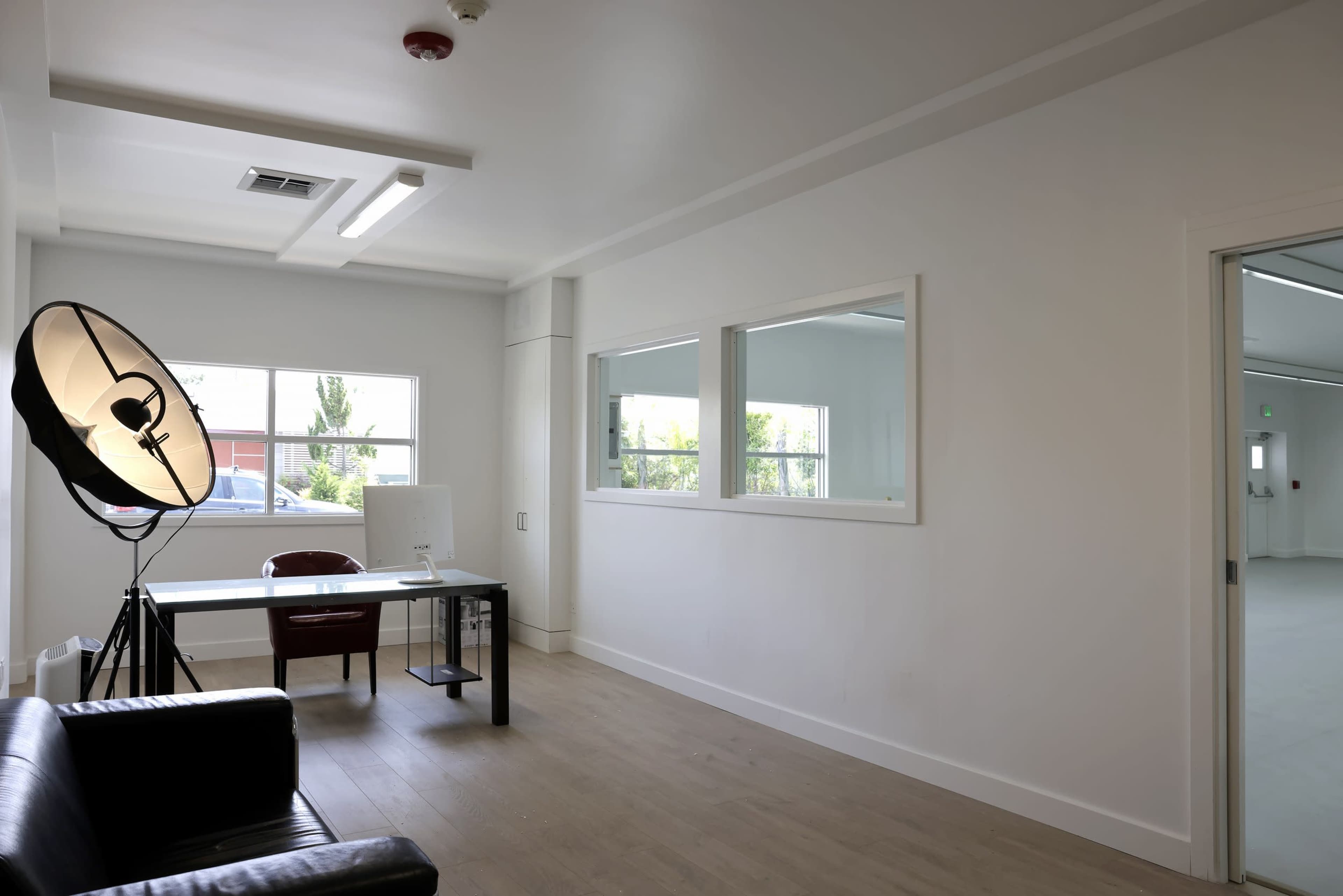 A bright, minimalist office space with a desk, a chair, and a large floor lamp, alongside a window offering natural light.