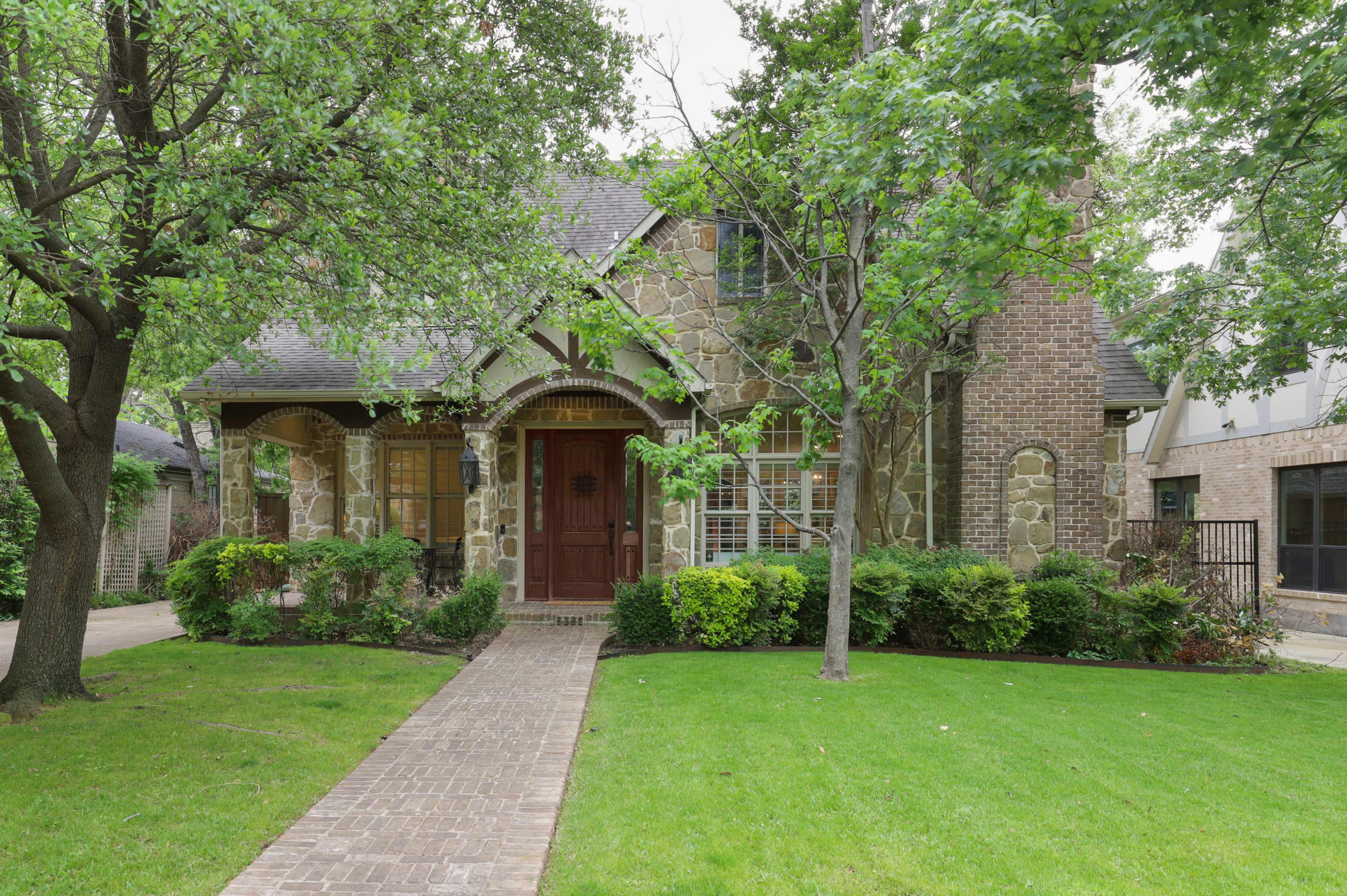 A stone and brick house features a landscaped front yard with a path leading to the entrance.