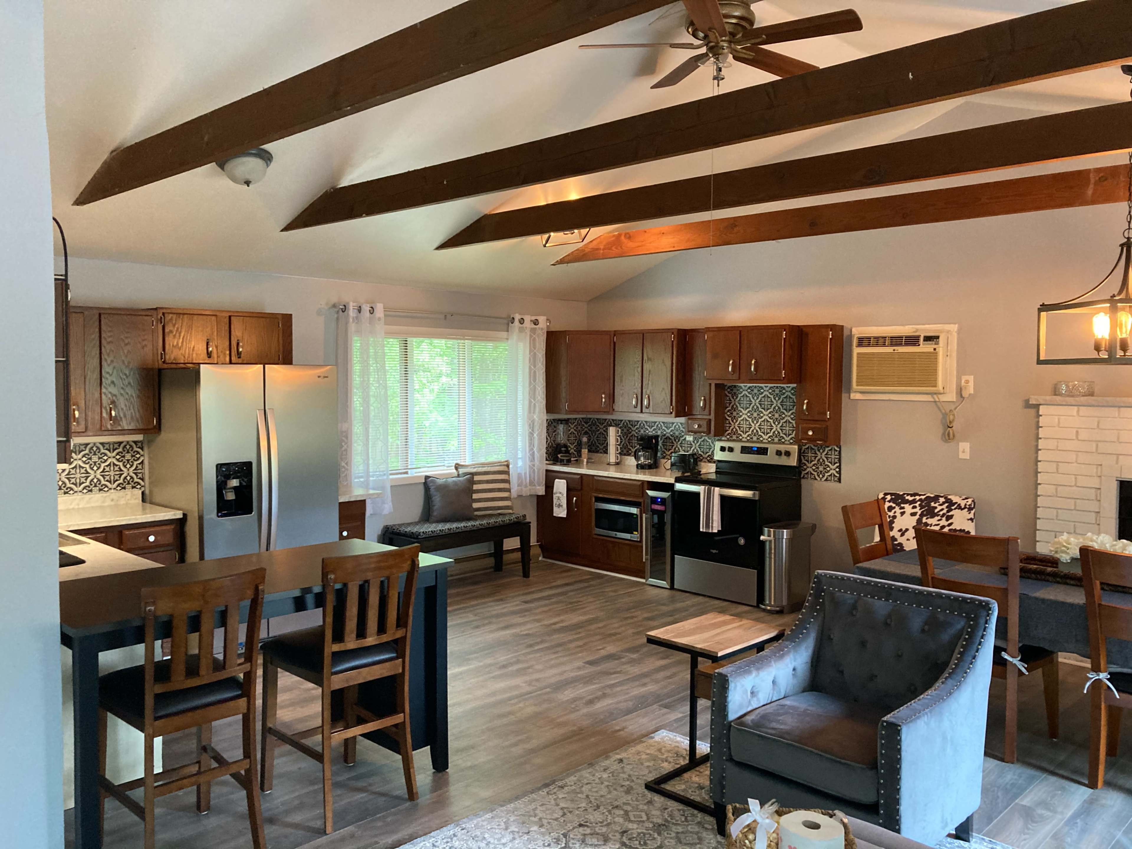 A modern open-concept kitchen and living area featuring wooden beams, a sink island, and a dining table with chairs.