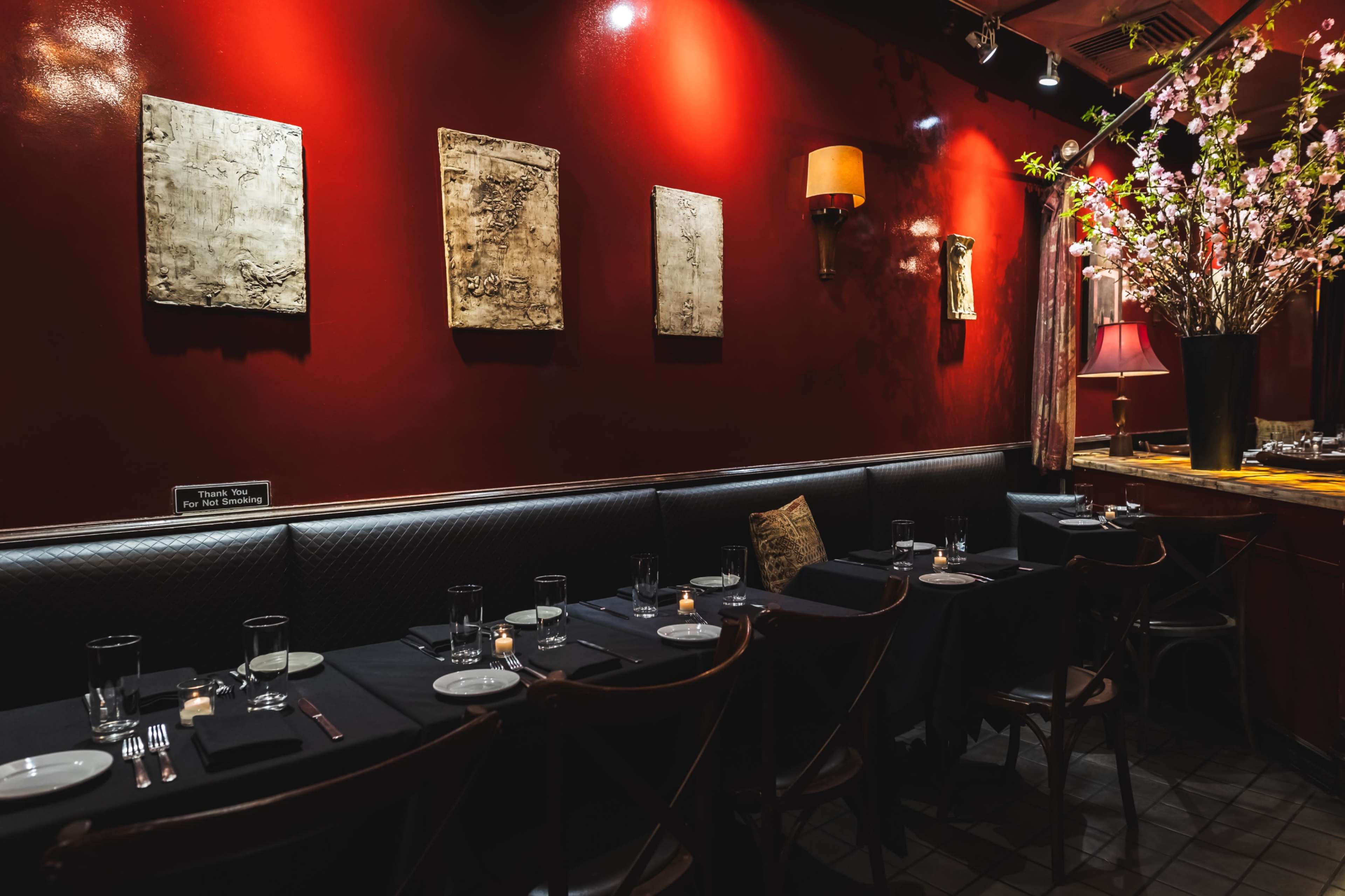 The image shows an intimate restaurant interior with dark red walls, black table settings, and decorative wall art.