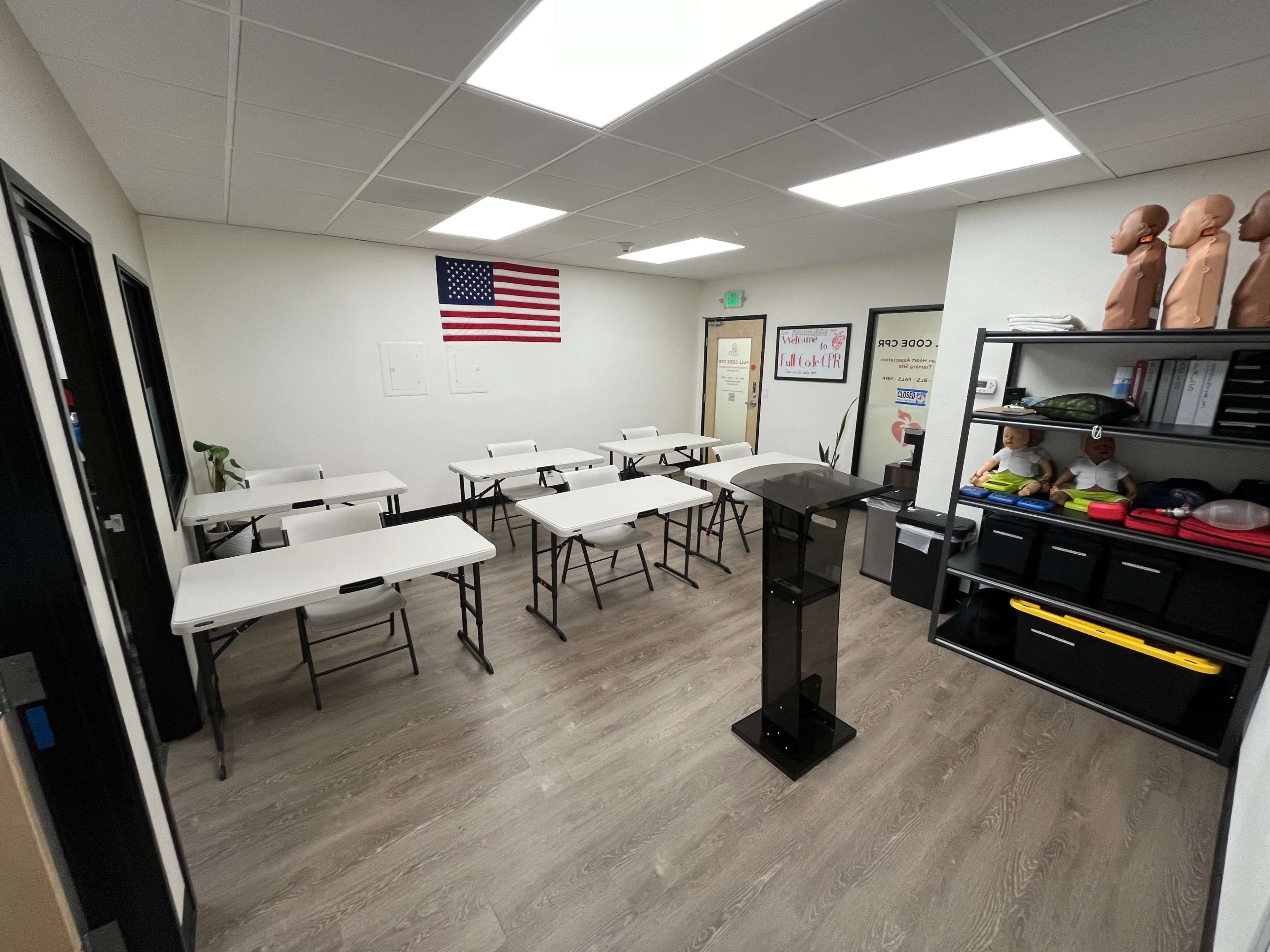A classroom with several folding tables arranged neatly, a podium at the front, and an American flag hanging on the wall.