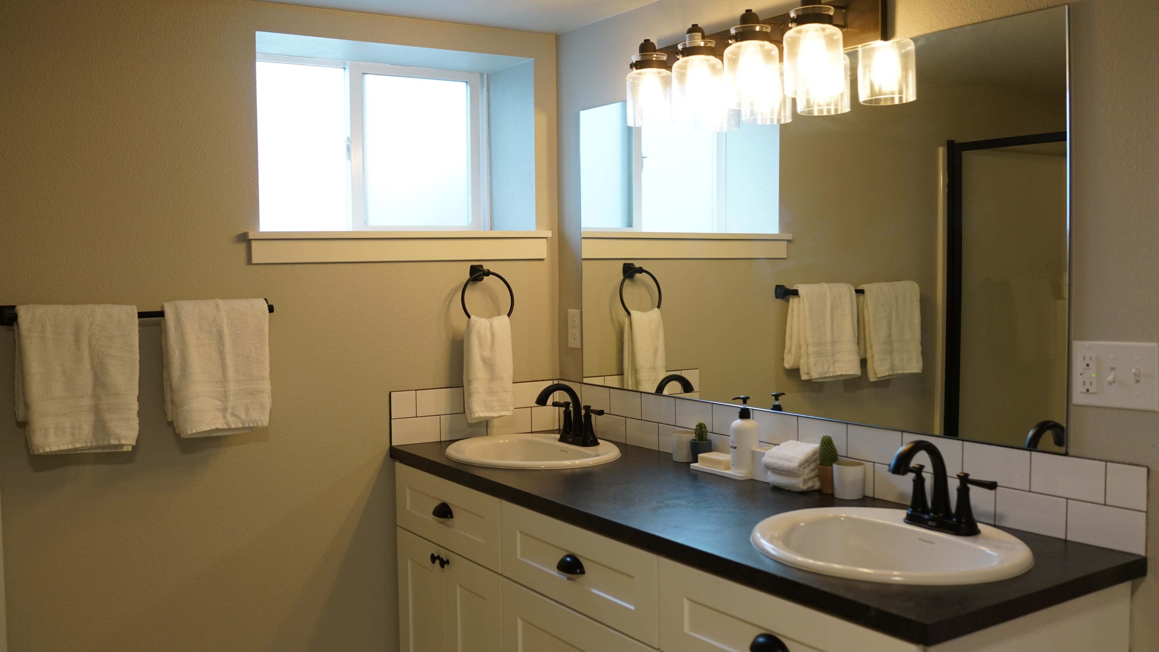 A modern bathroom featuring a double sink vanity with black faucets, two mirrors, and a well-lit area with four hanging light fixtures.