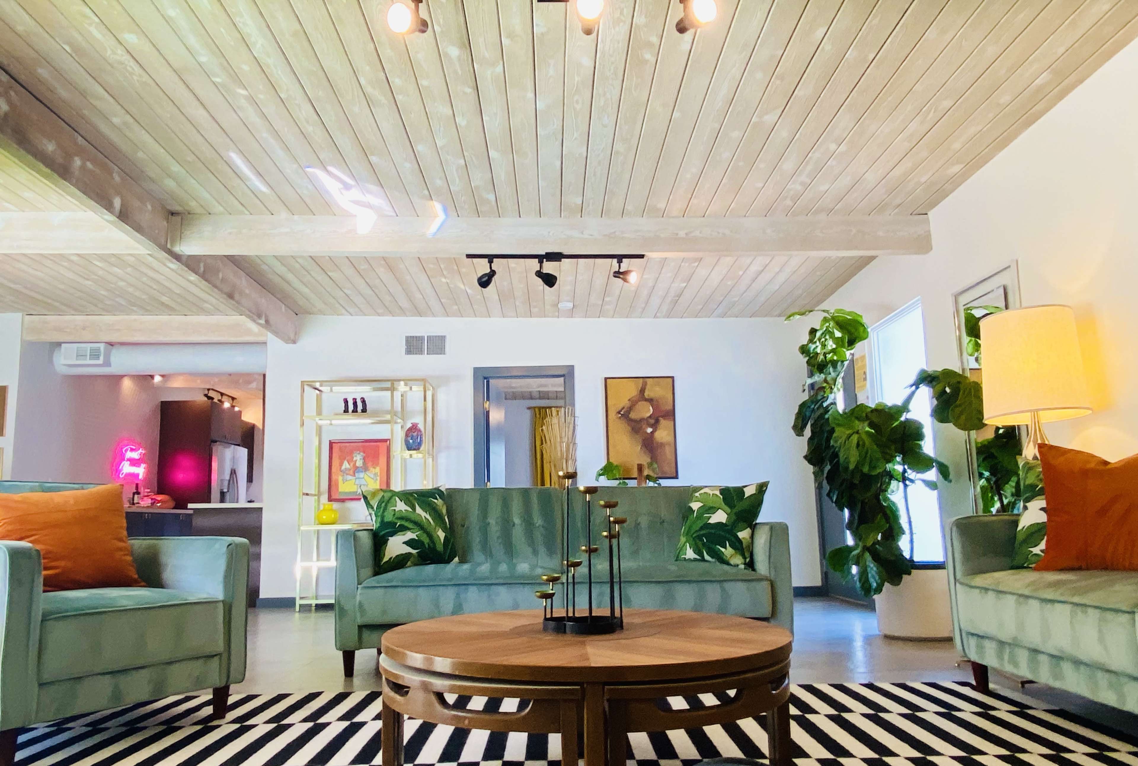 A modern living space with two green sofas, a round wooden coffee table, and a striped rug, characterized by wooden beams and bright decor elements.