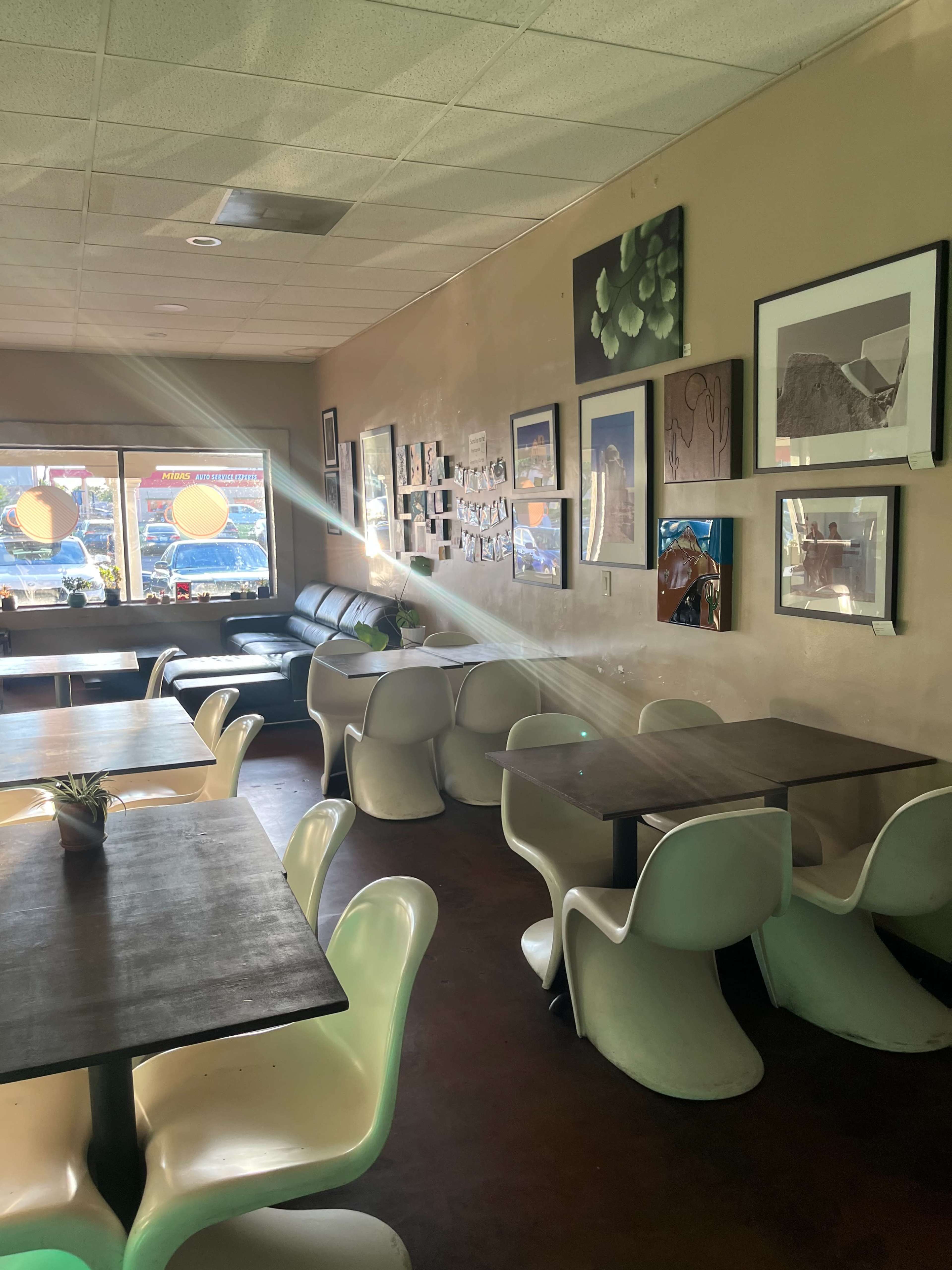 A cozy café interior with wooden tables, white chairs, and walls adorned with various framed artworks.
