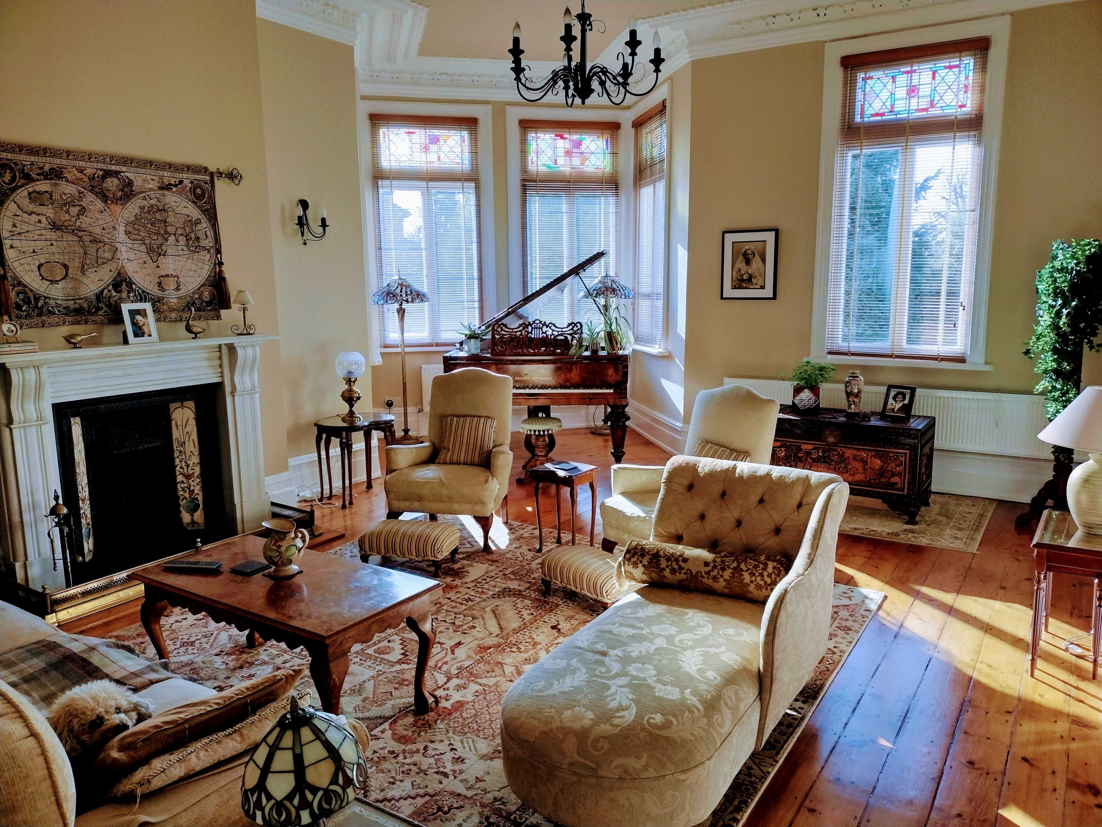 A well-furnished living room with a piano, ornate furniture, a large rug, and decorative stained glass windows.