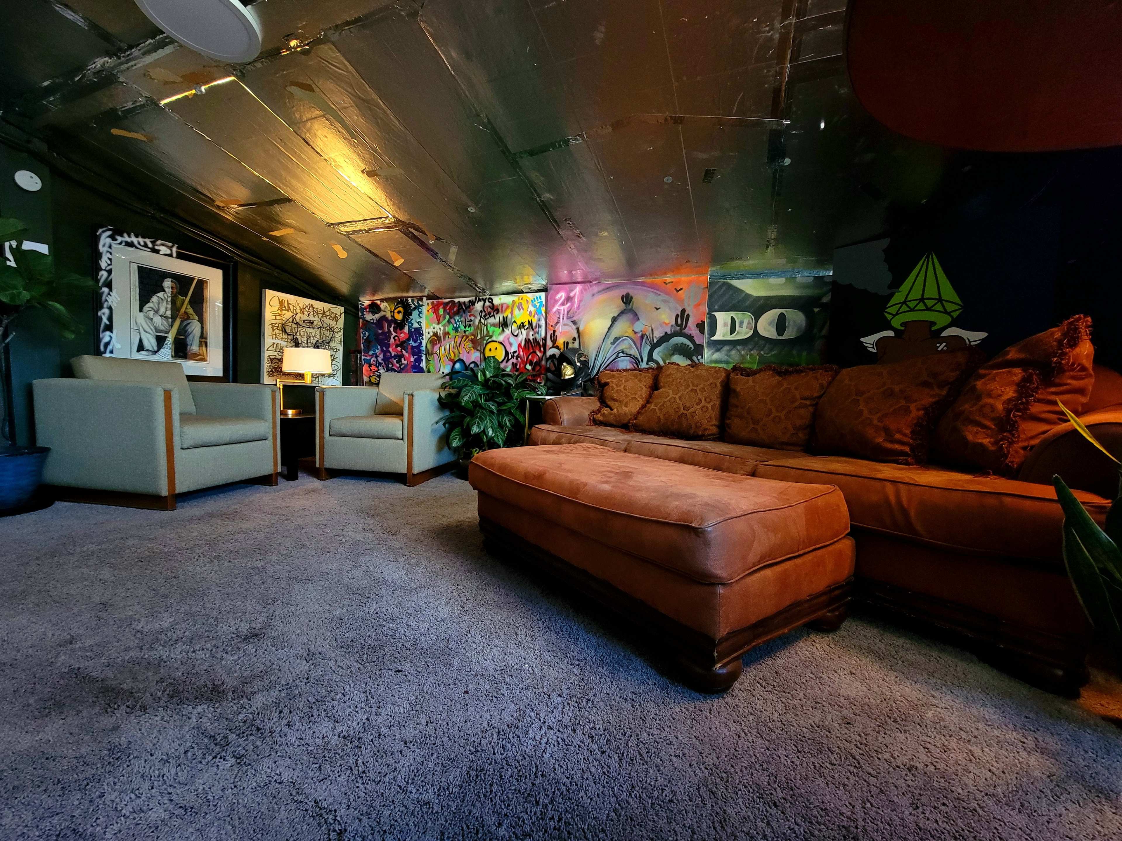 A cozy attic space with a brown couch, two armchairs, and colorful graffiti artwork on the walls.