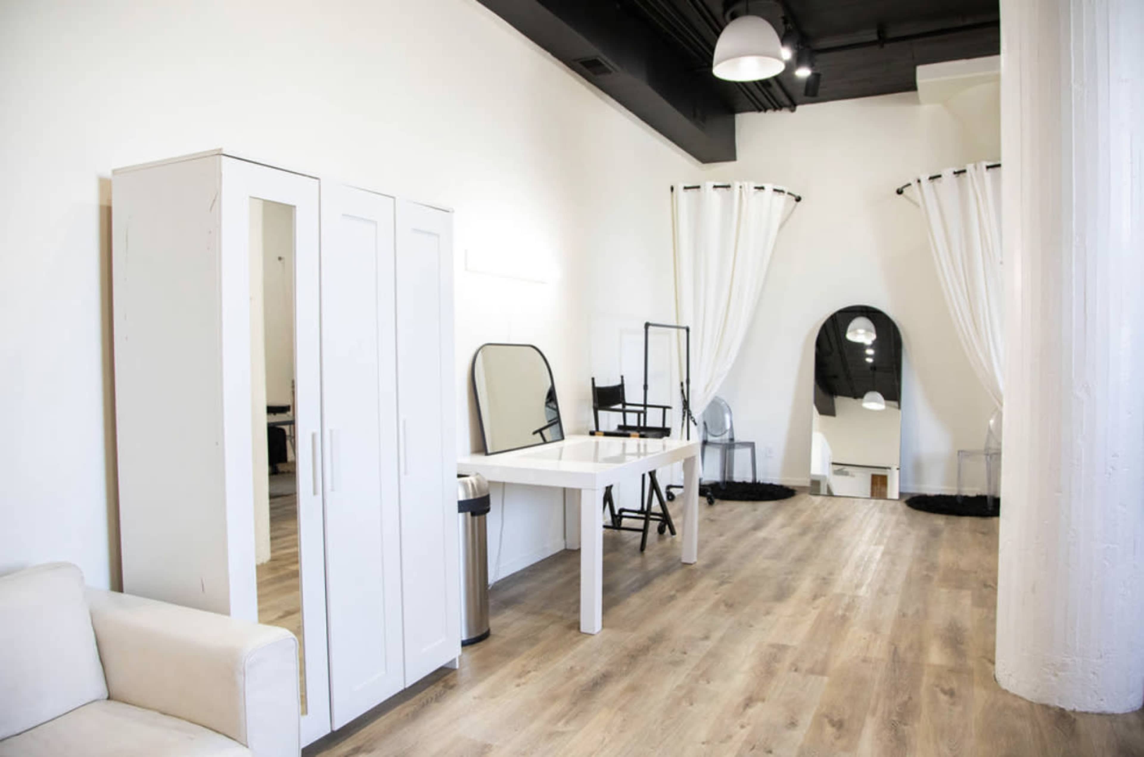 A bright, minimalist interior of a room featuring a white wardrobe, mirrors, a table, and light curtains.