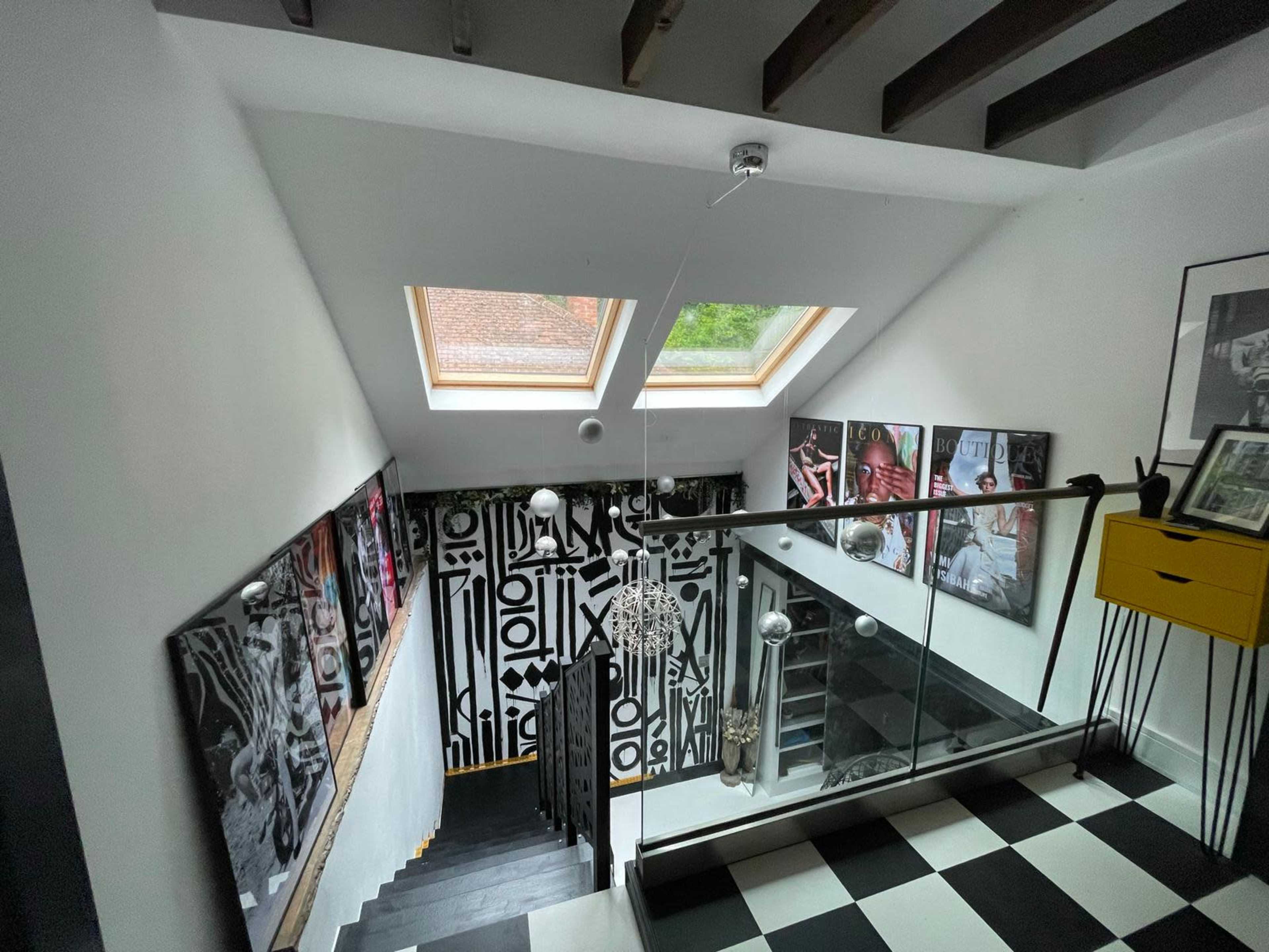 A staircase with a black and white checkered floor features large framed photographs on the walls and skylights above, leading down to a lower level.