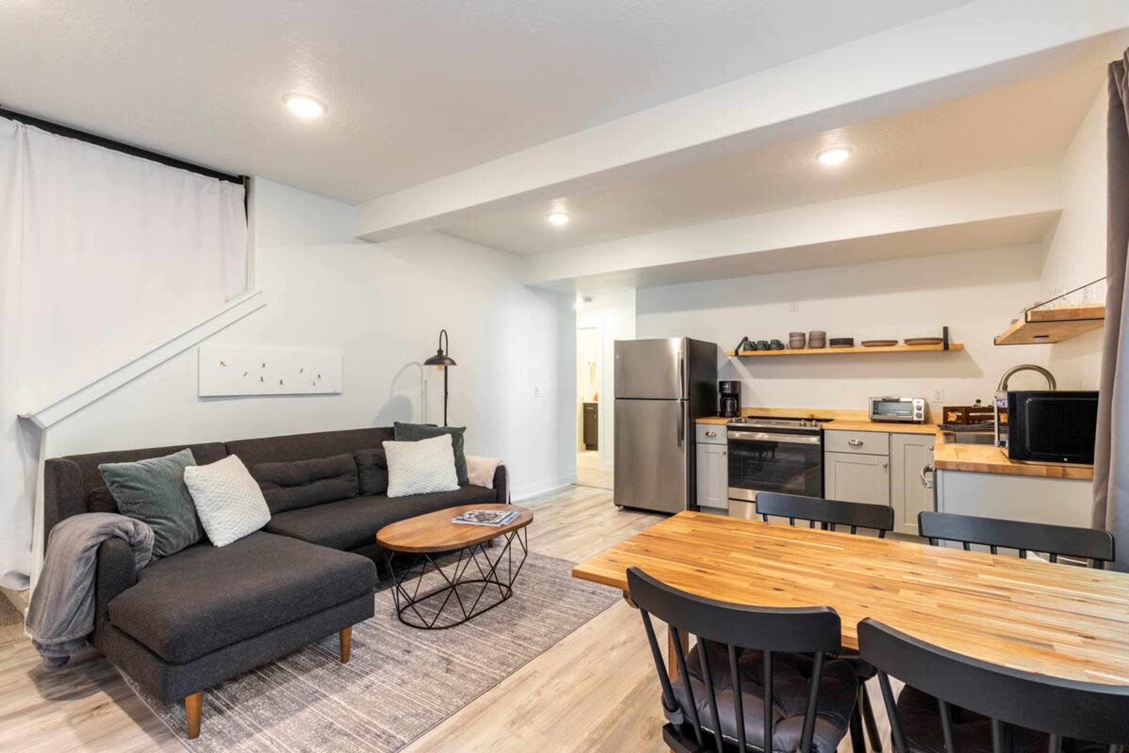 A modern, open-concept living area with a sofa, coffee table, dining table, and kitchen appliances.