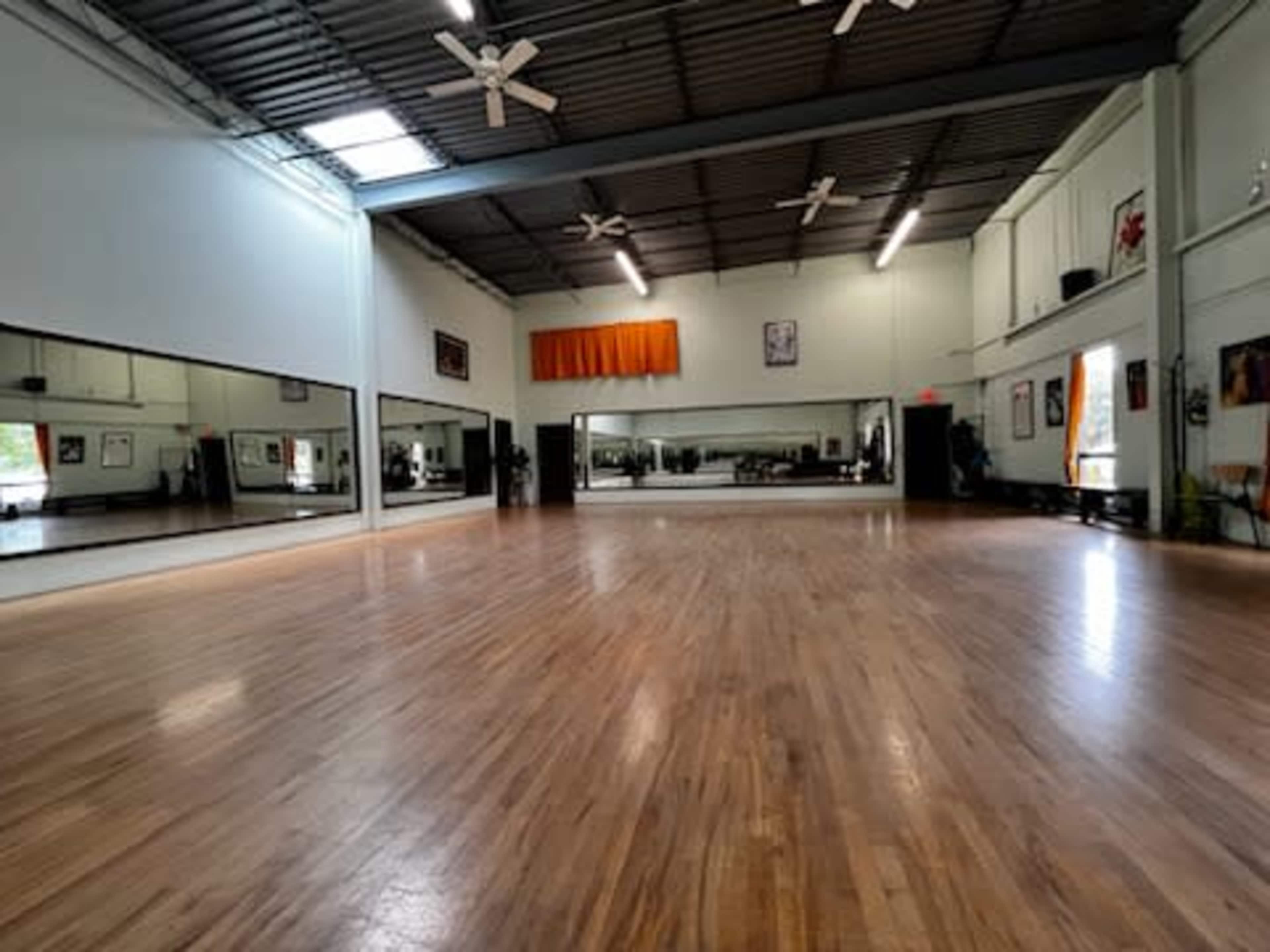 A spacious dance studio featuring wooden floors, large mirrors on one wall, and ceiling fans.