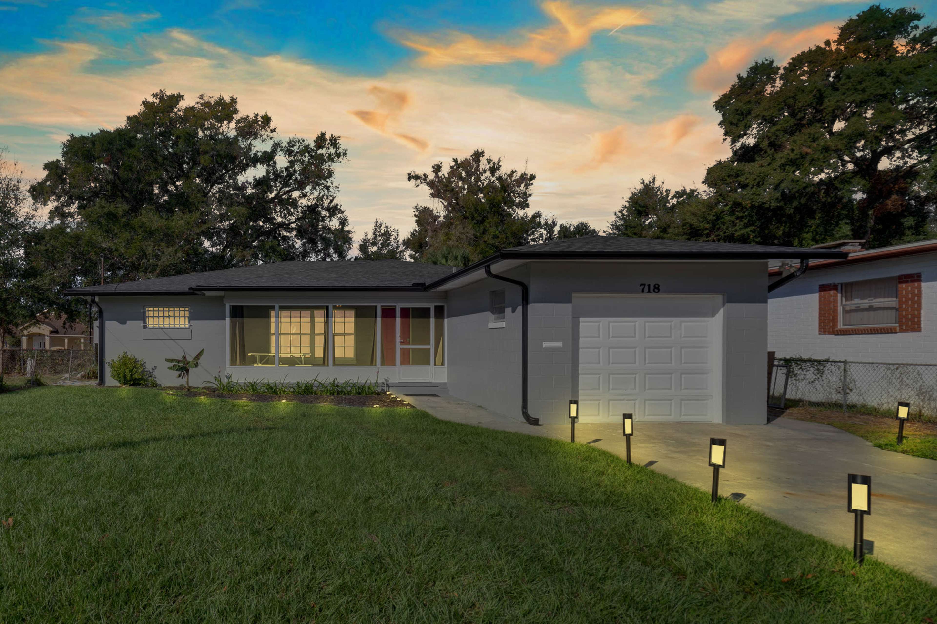 A modern single-story house with a gray exterior, a attached garage, and a landscaped front yard, illuminated by pathway lights.