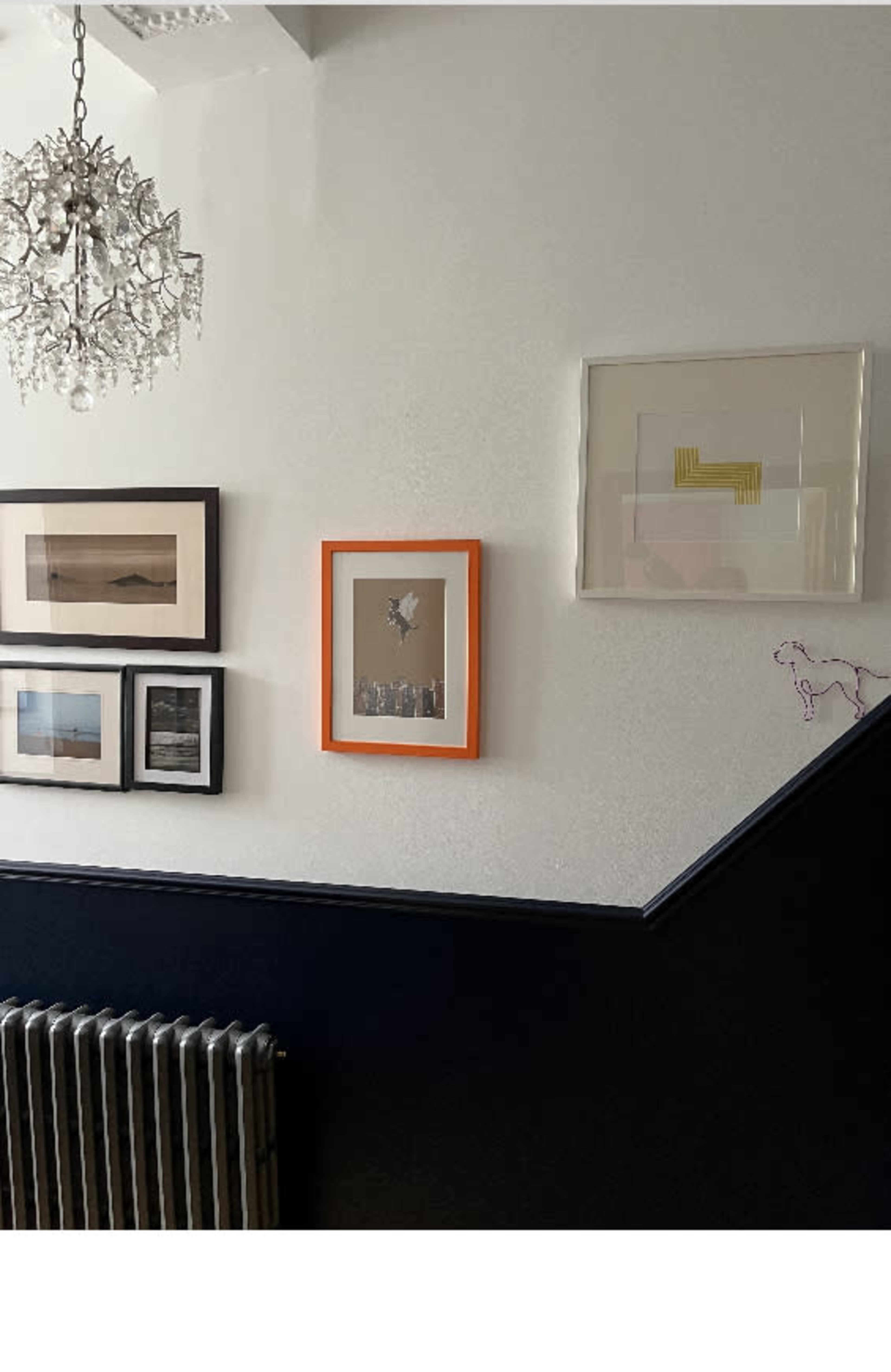 A wall with framed pictures in various styles and a decorative chandelier above, along with an exposed radiator along the bottom.