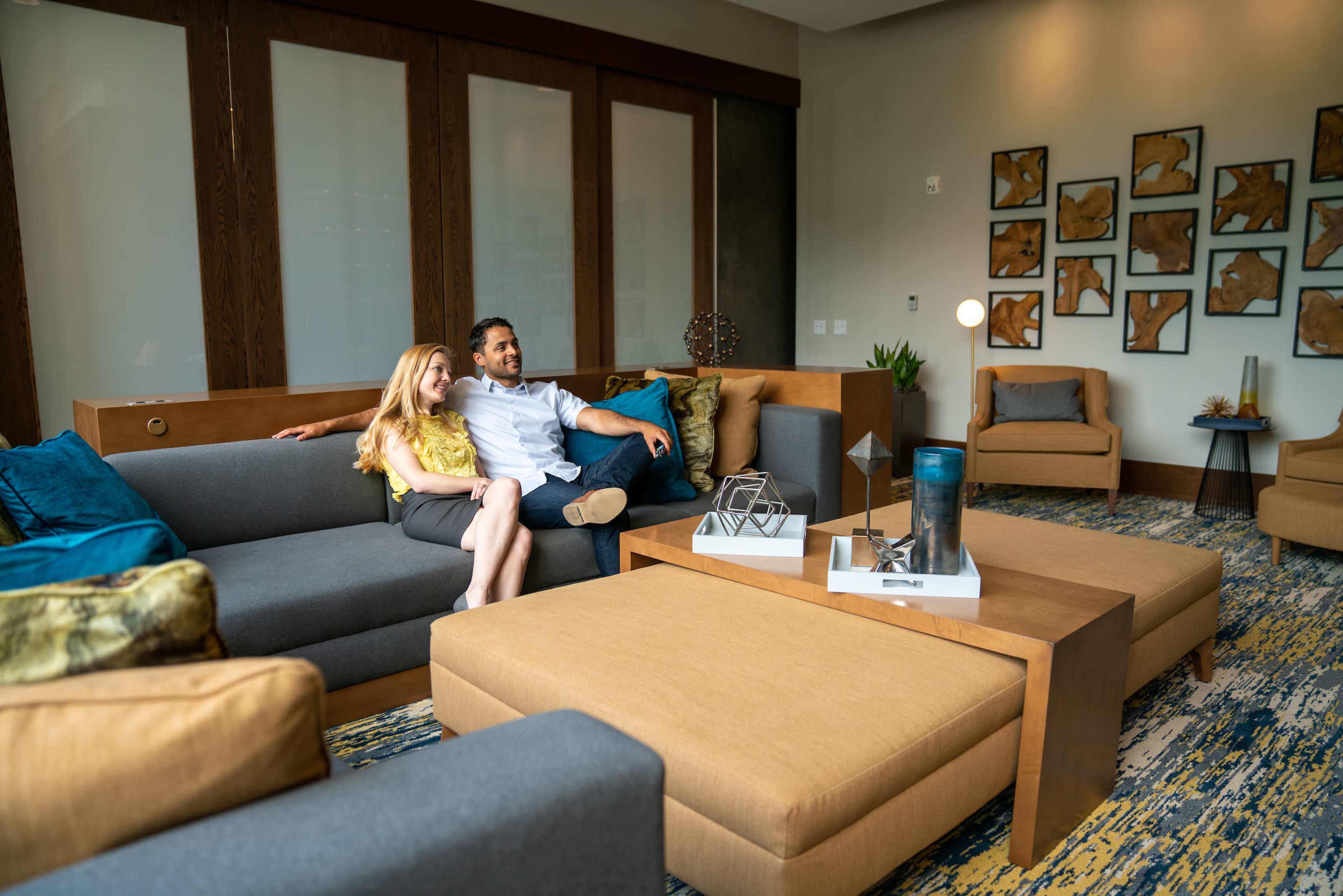 A couple sits together on a large sectional sofa in a modern lounge area with artwork on the walls.