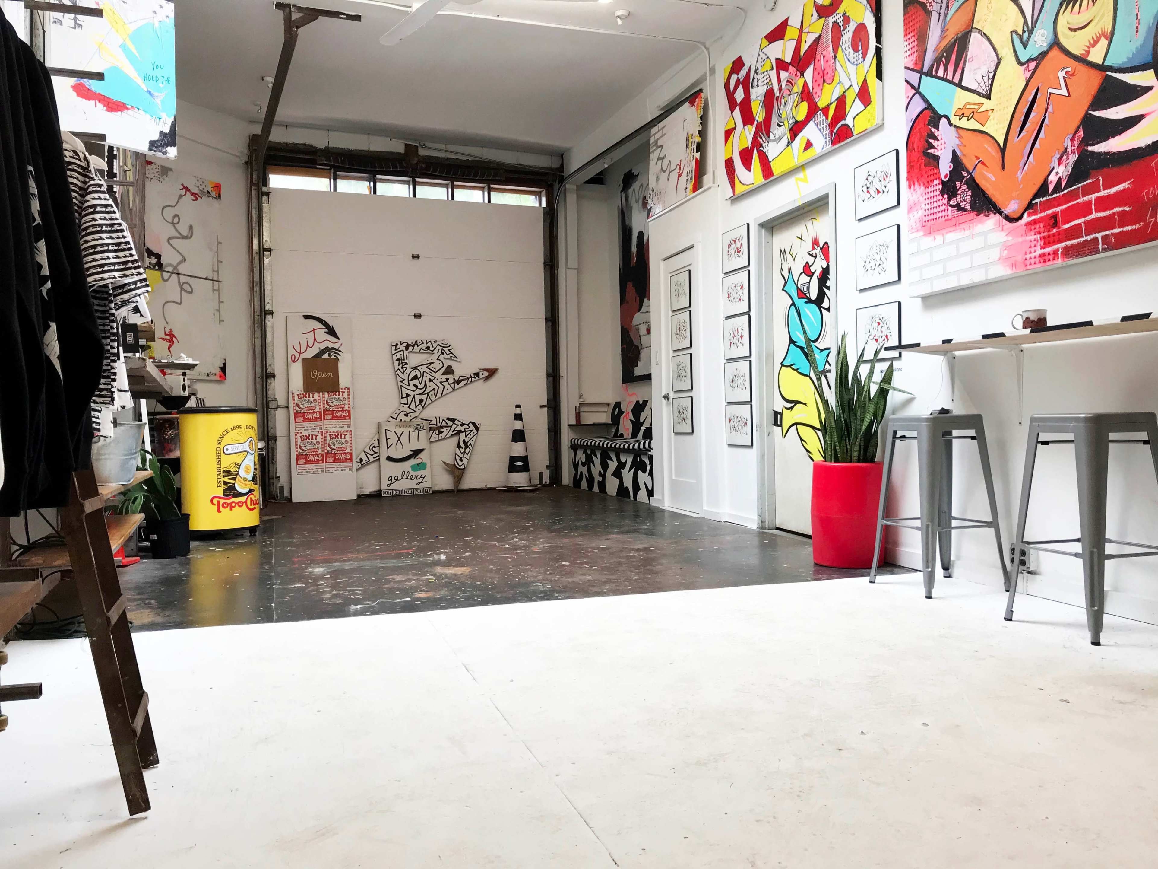 An art studio with exposed walls, a polished concrete floor, and various artworks displayed on the walls.