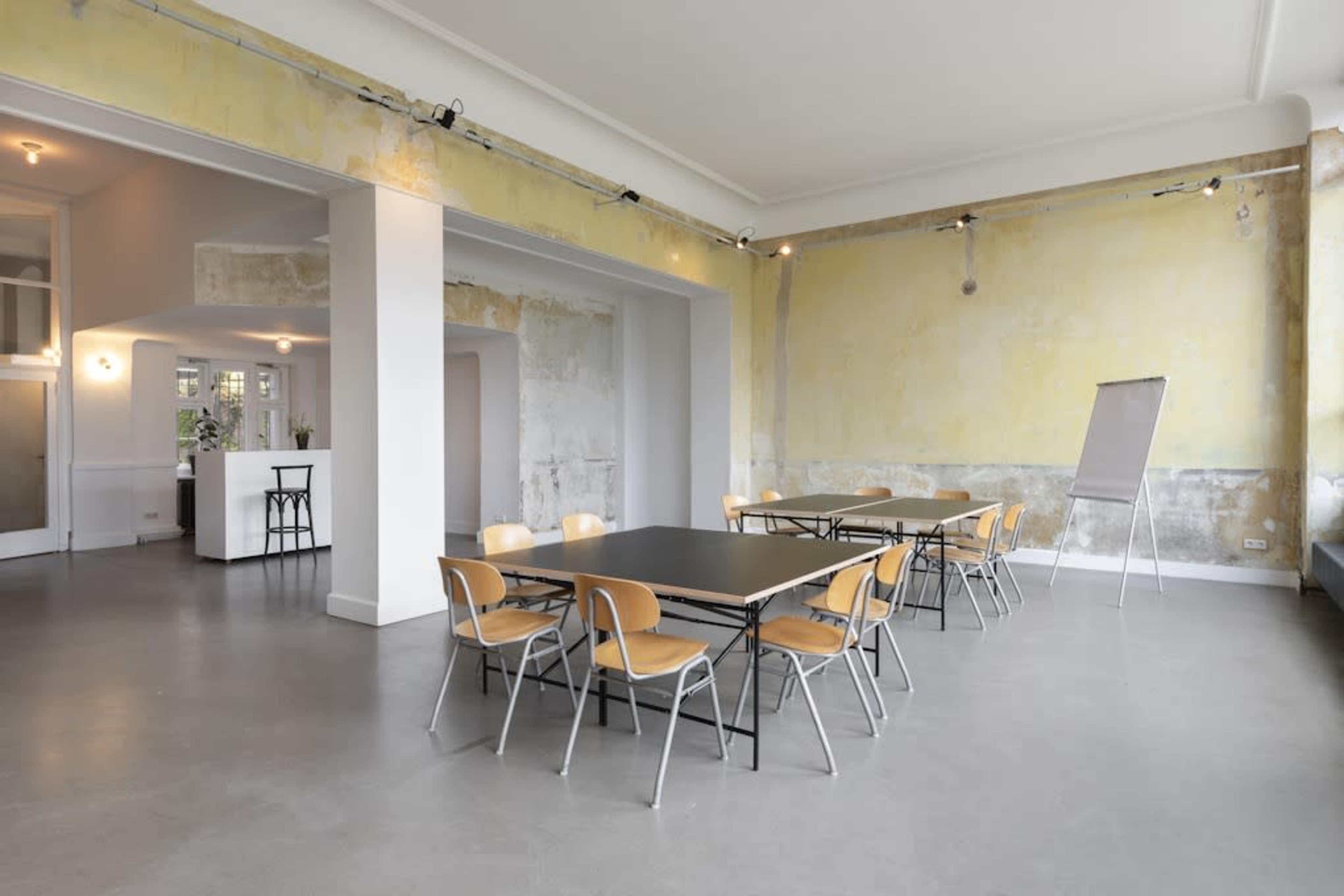 A modern, unfinished interior space features a series of black tables surrounded by wooden chairs on a concrete floor.