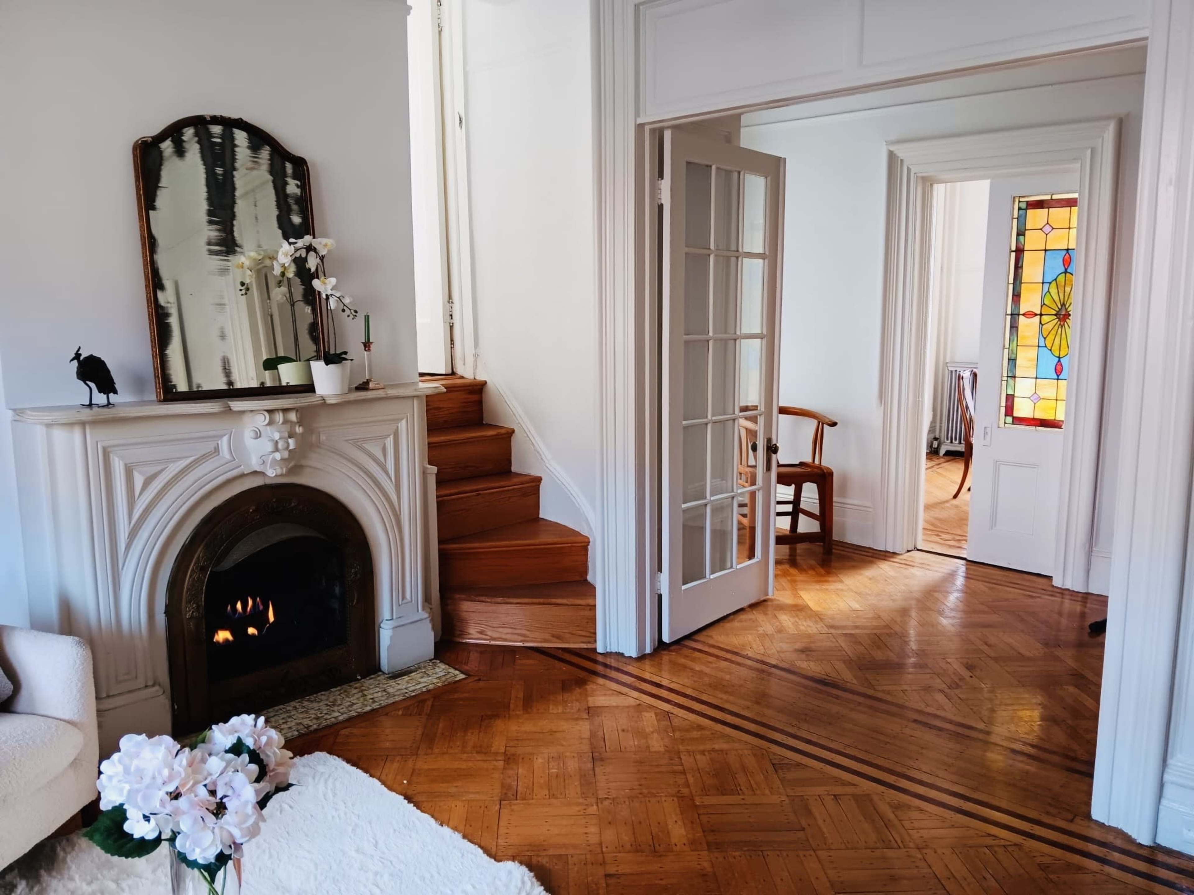 A room with a decorative fireplace, a staircase leading upwards, and a stained glass window illuminating adjacent spaces.