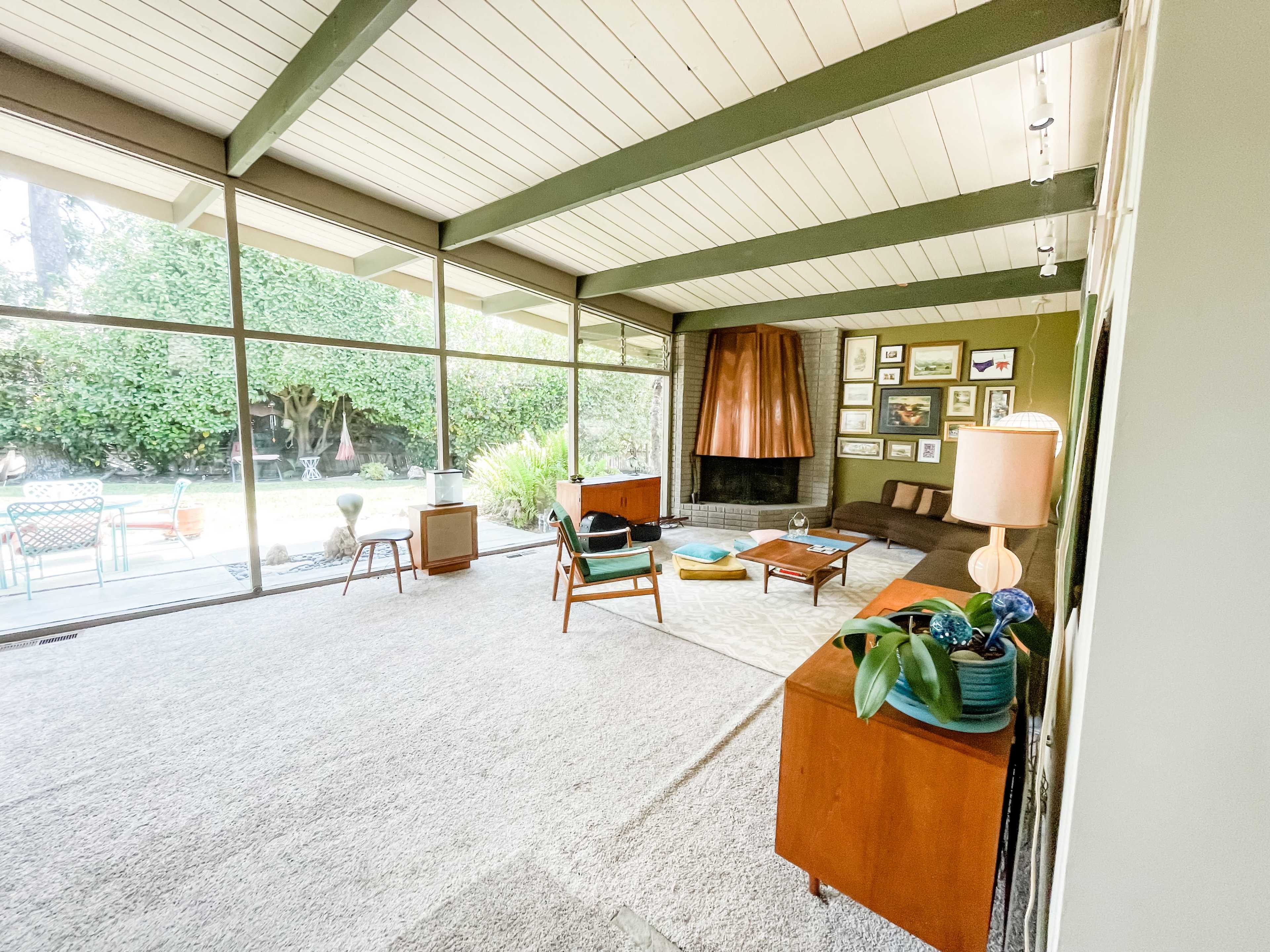 The image showcases a mid-century modern living room with large glass windows, a stone fireplace, and stylish furniture arrangements.