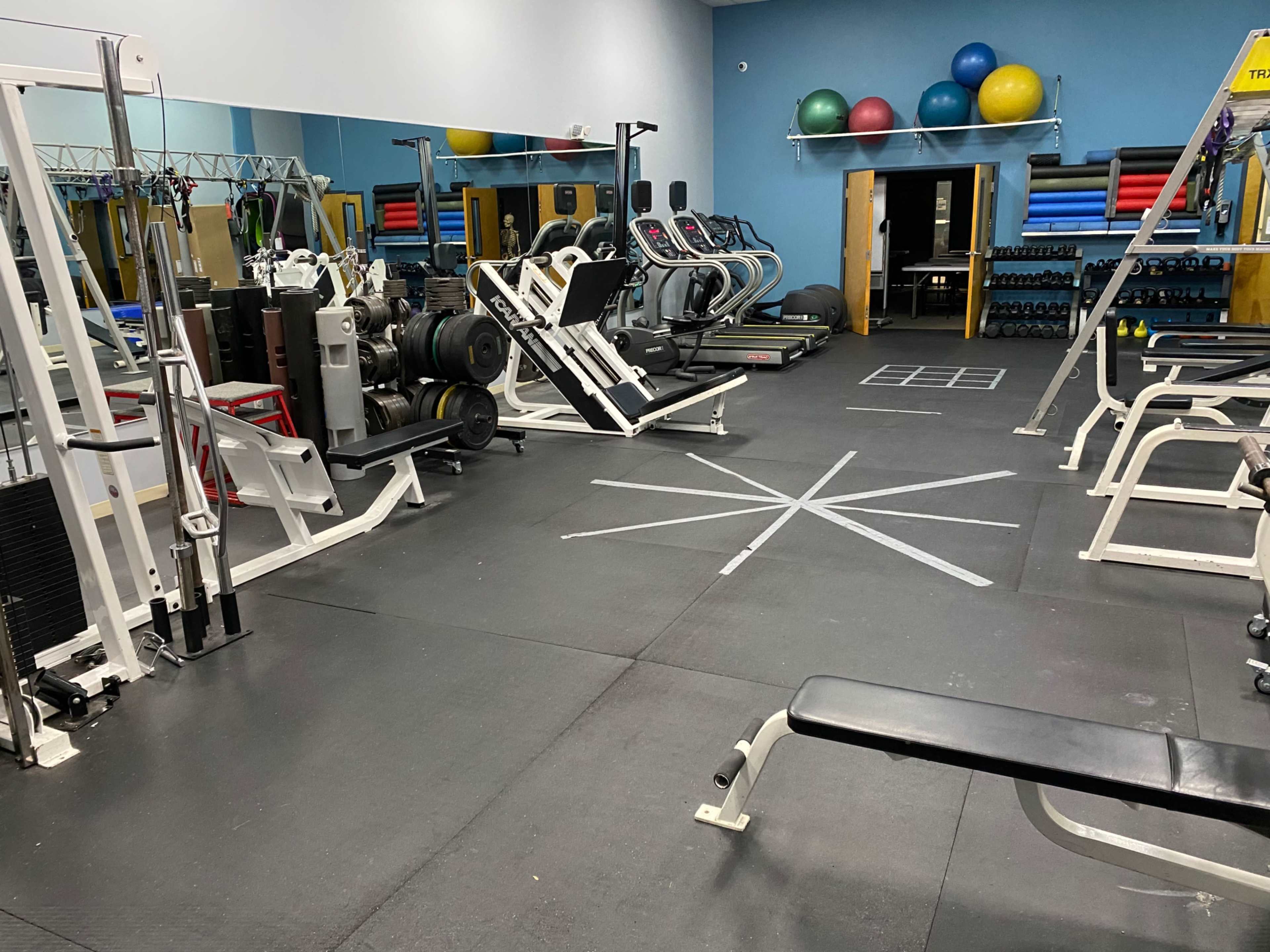 A gym with various exercise equipment, including weight machines, cardio machines, and free weights, arranged in a spacious layout.