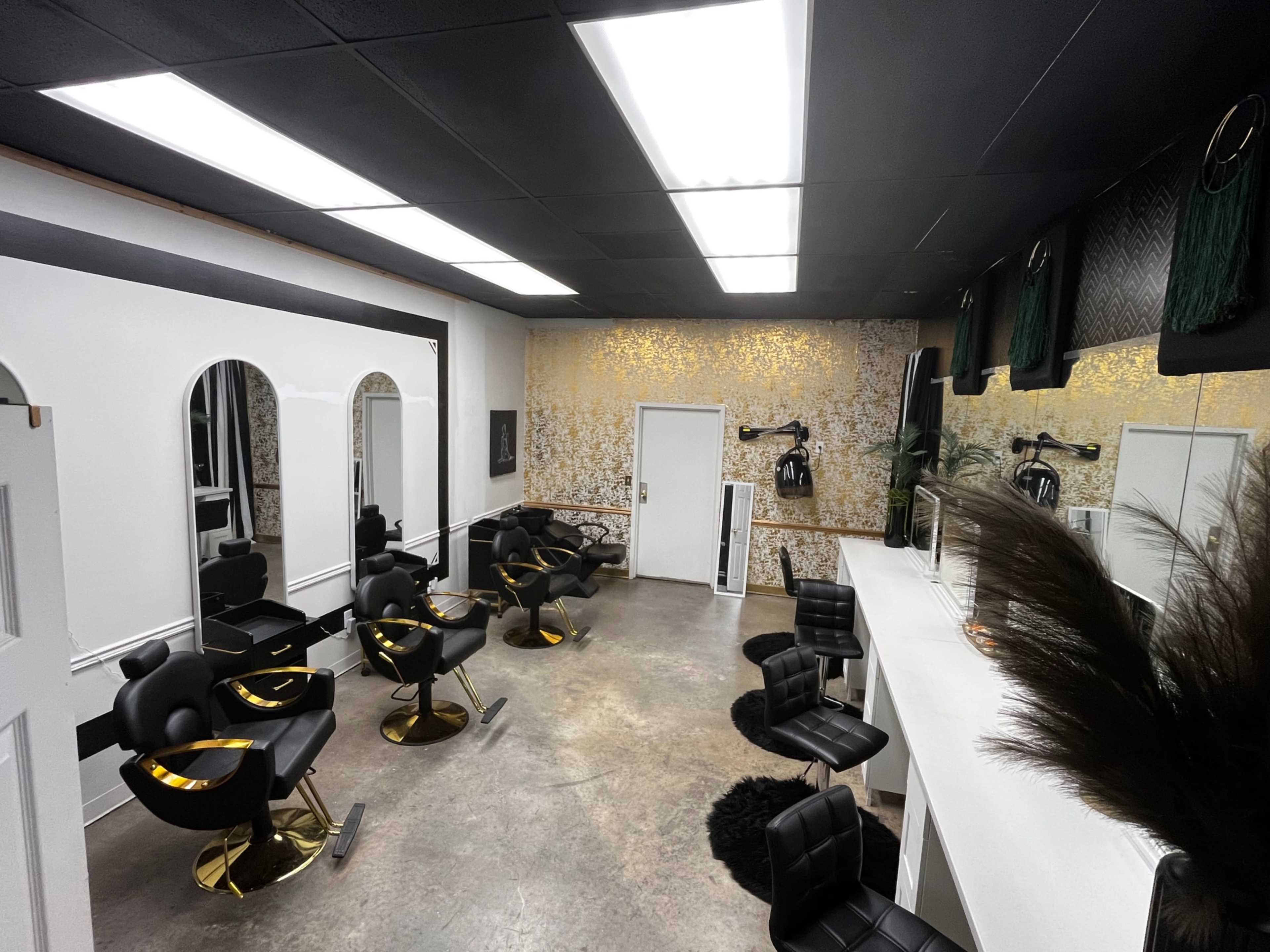 The image shows a modern hair salon with black salon chairs, large mirrors, and a gold-accented wall.