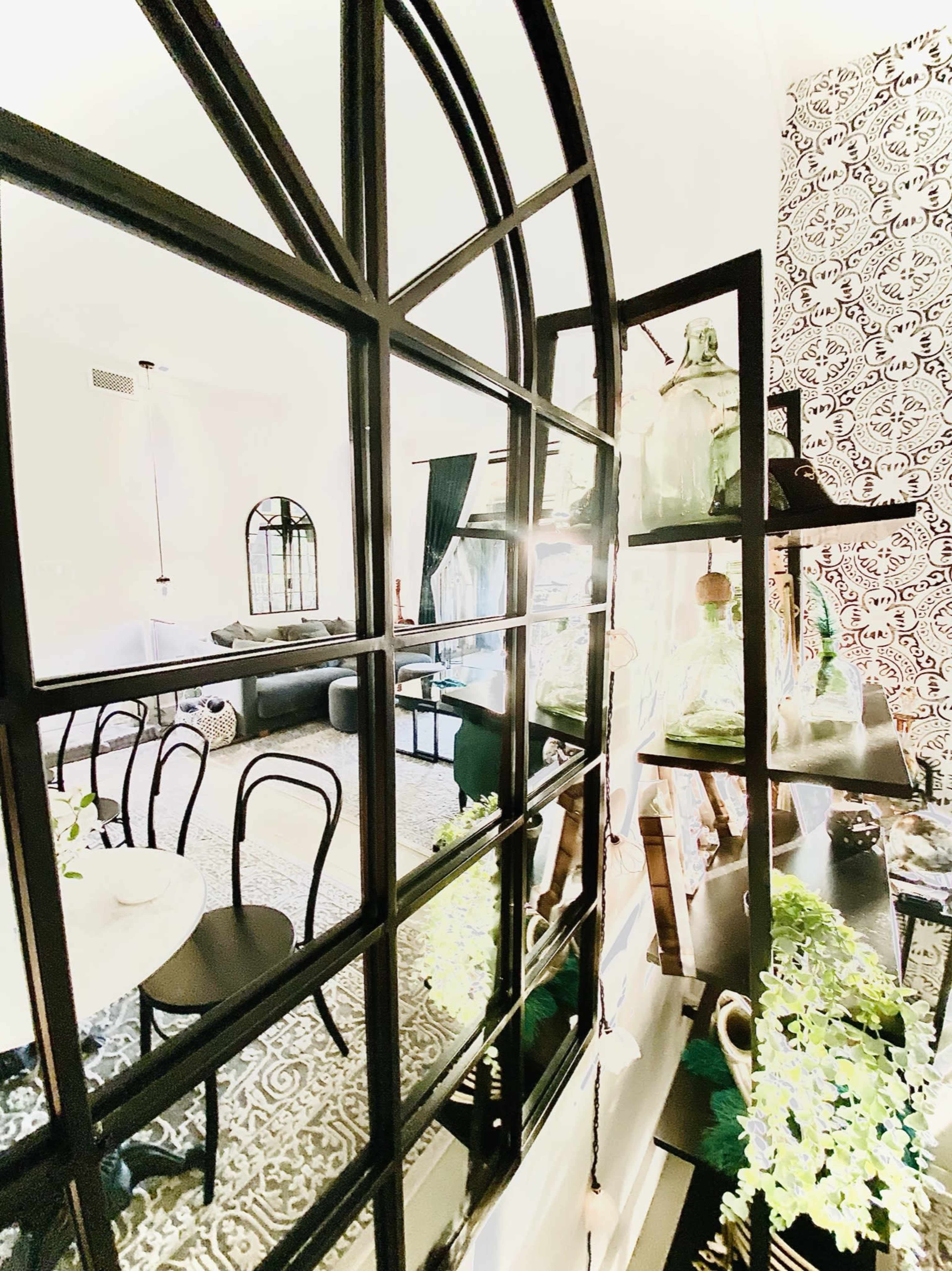 A room featuring a large black-framed mirror reflecting a decorated living space with plants and patterned wallpaper.