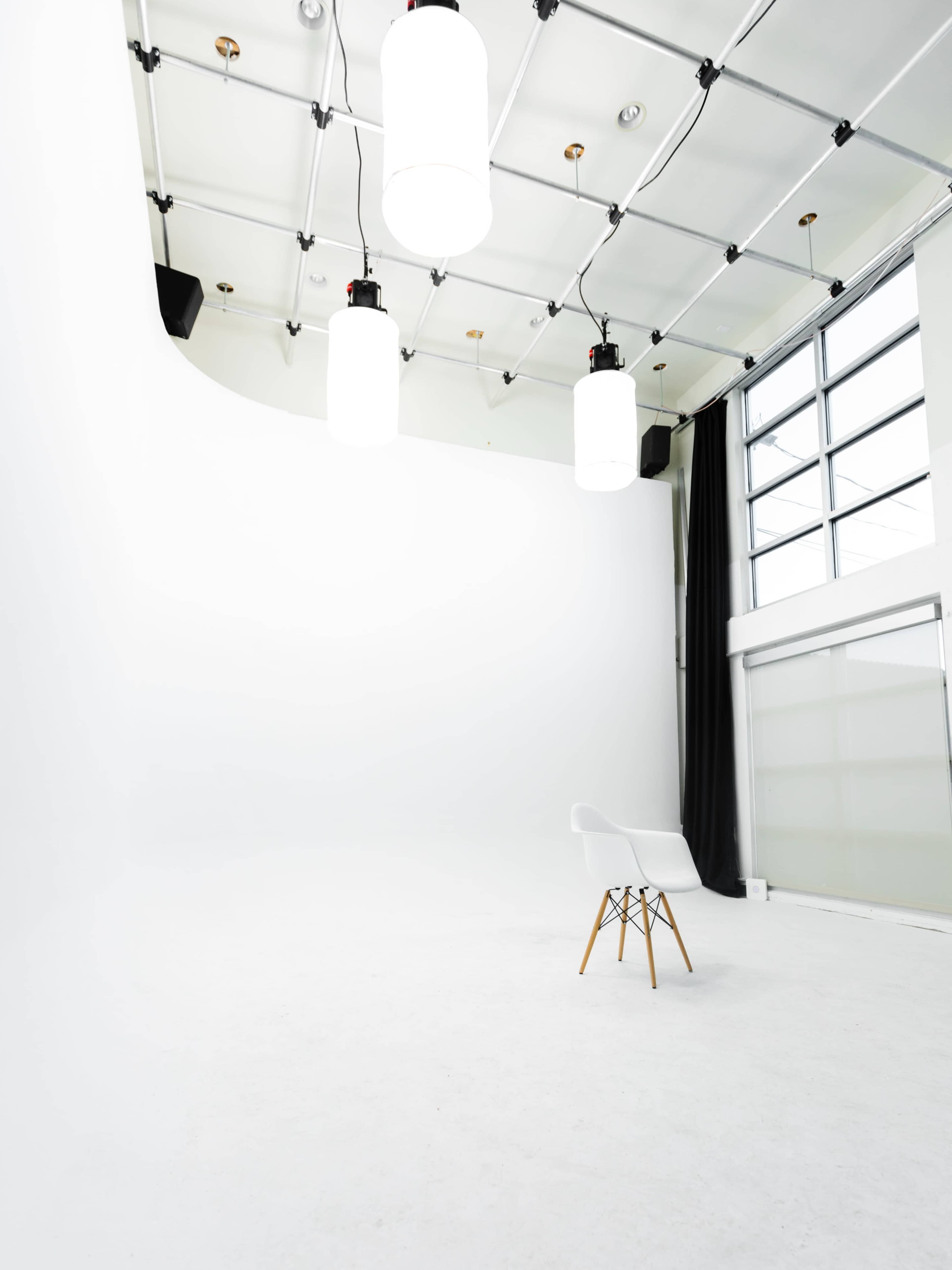 A minimalistic white studio space with a single chair in the center and large pendant lights hanging from the ceiling.
