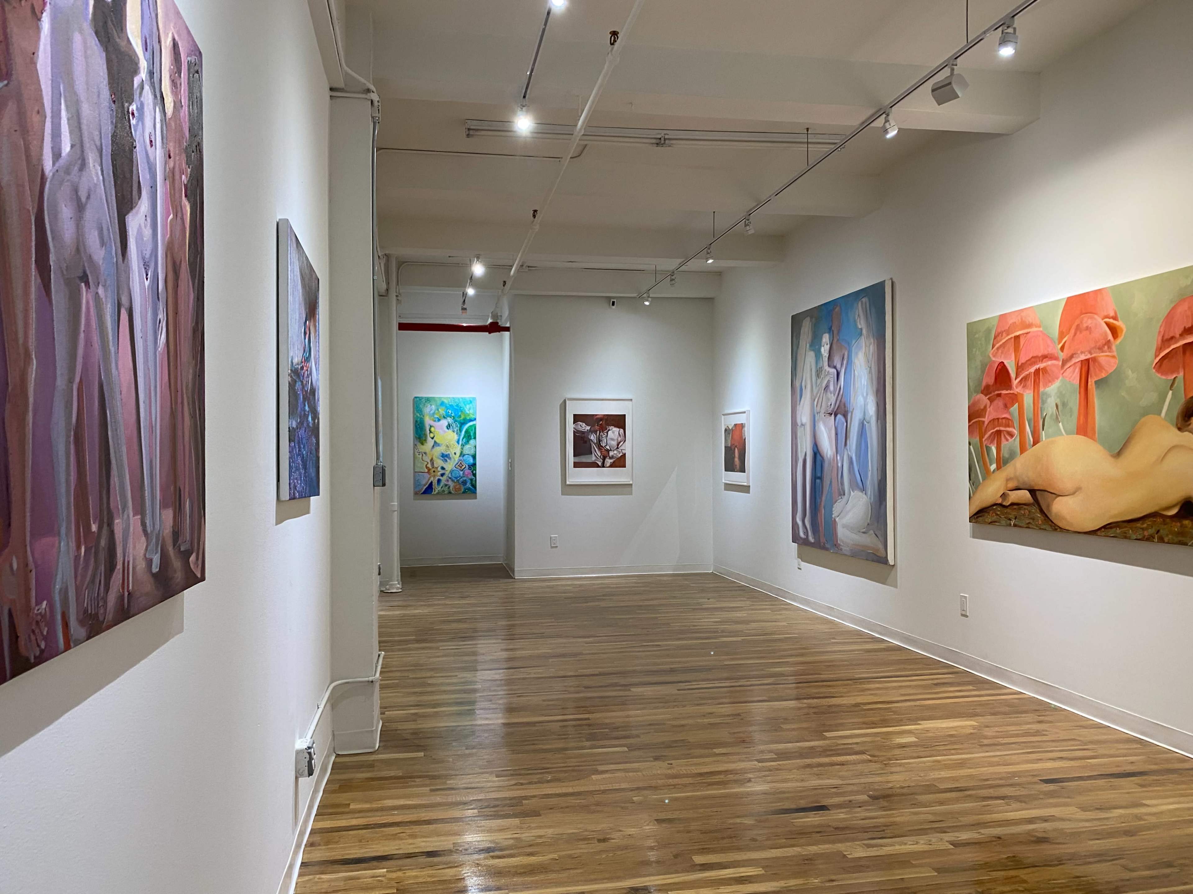 An art gallery with several large paintings on the walls and wooden flooring.