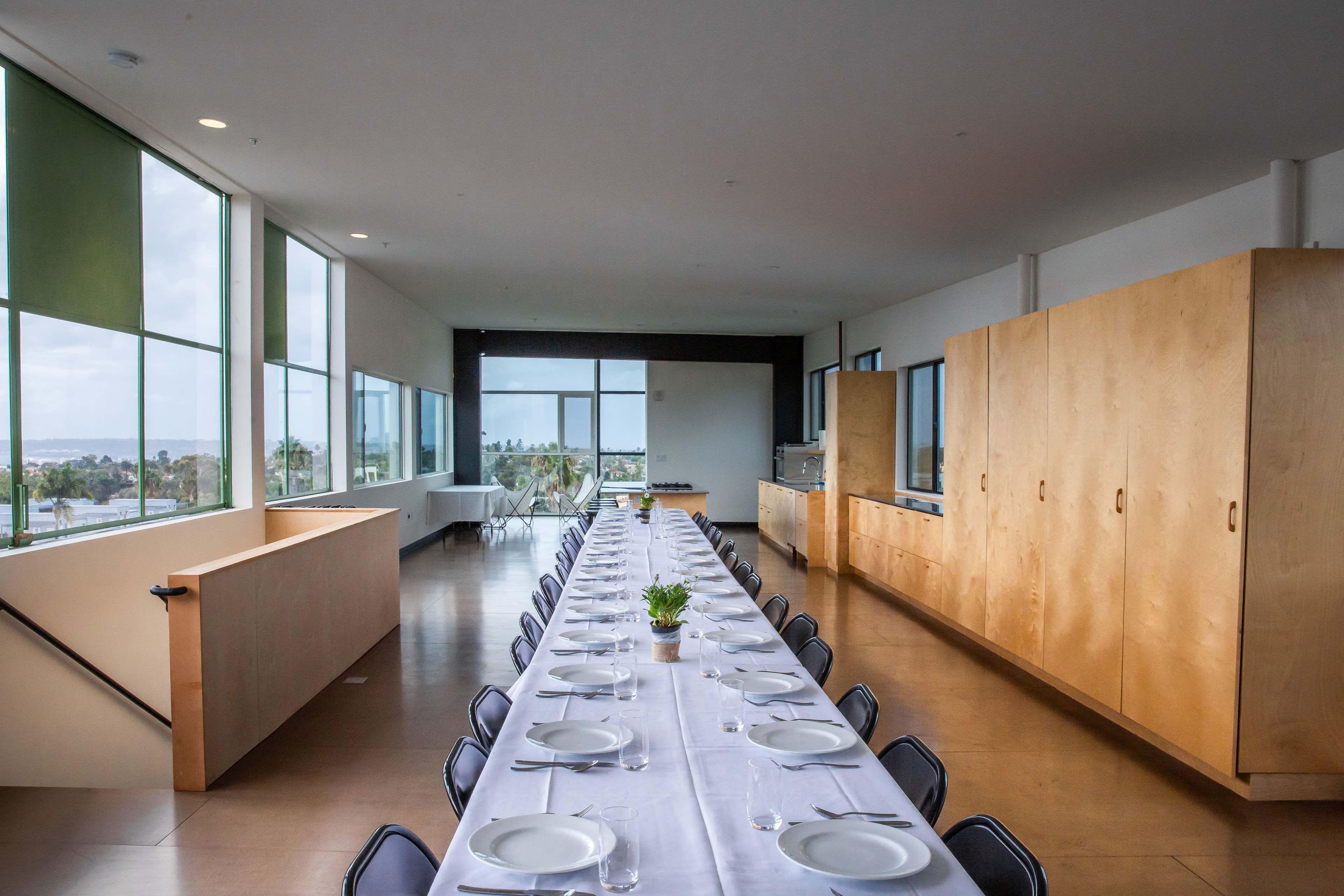 A long dining table is set for a meal in a spacious room with large windows overlooking a view.