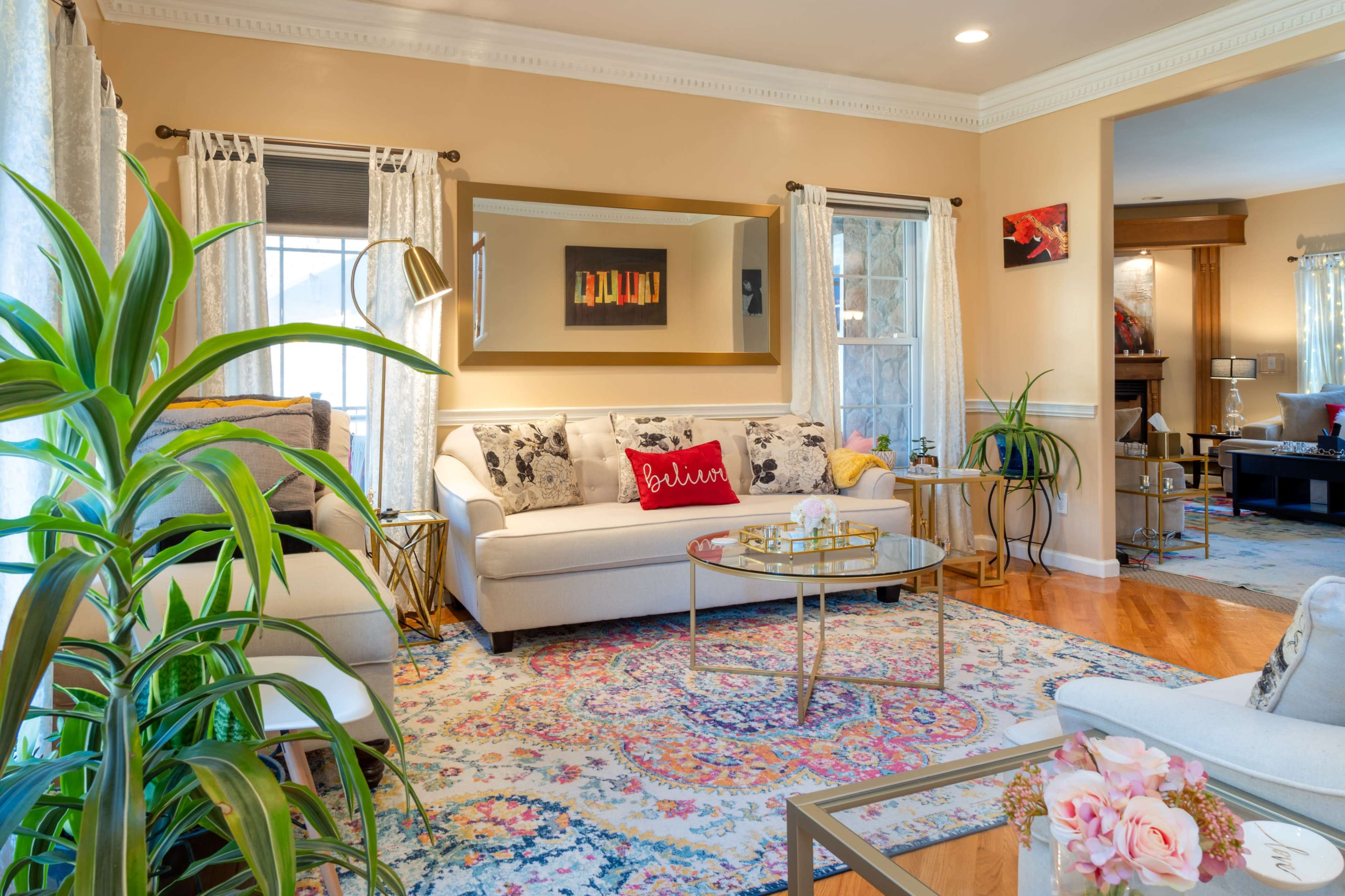 The living room features a light-colored sofa, a round coffee table, and decorative plants, with a colorful area rug covering the hardwood floor.