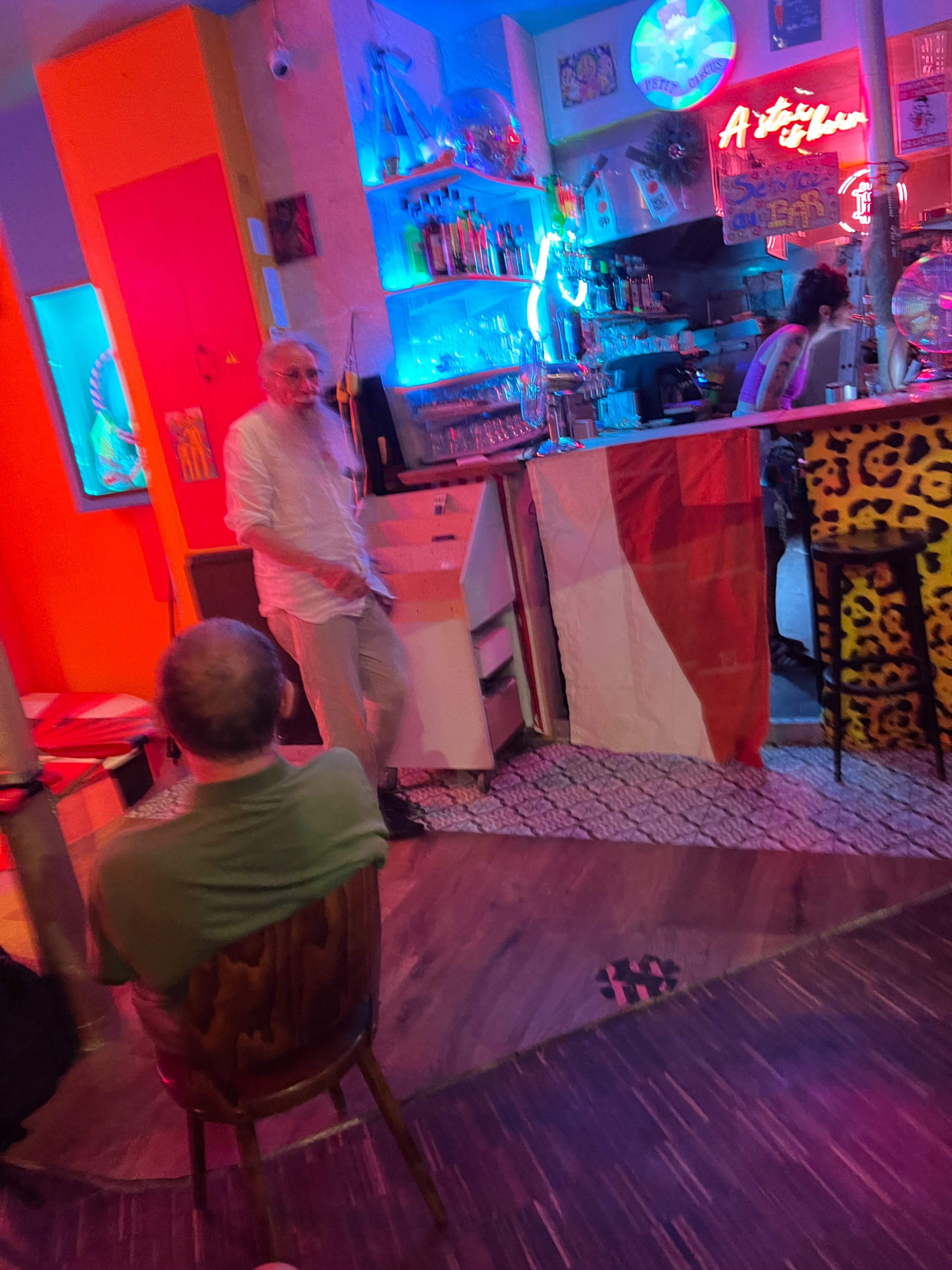 A lively bar scene features a colorful interior with bright neon lights and a bartender behind the counter, while patrons sit nearby.