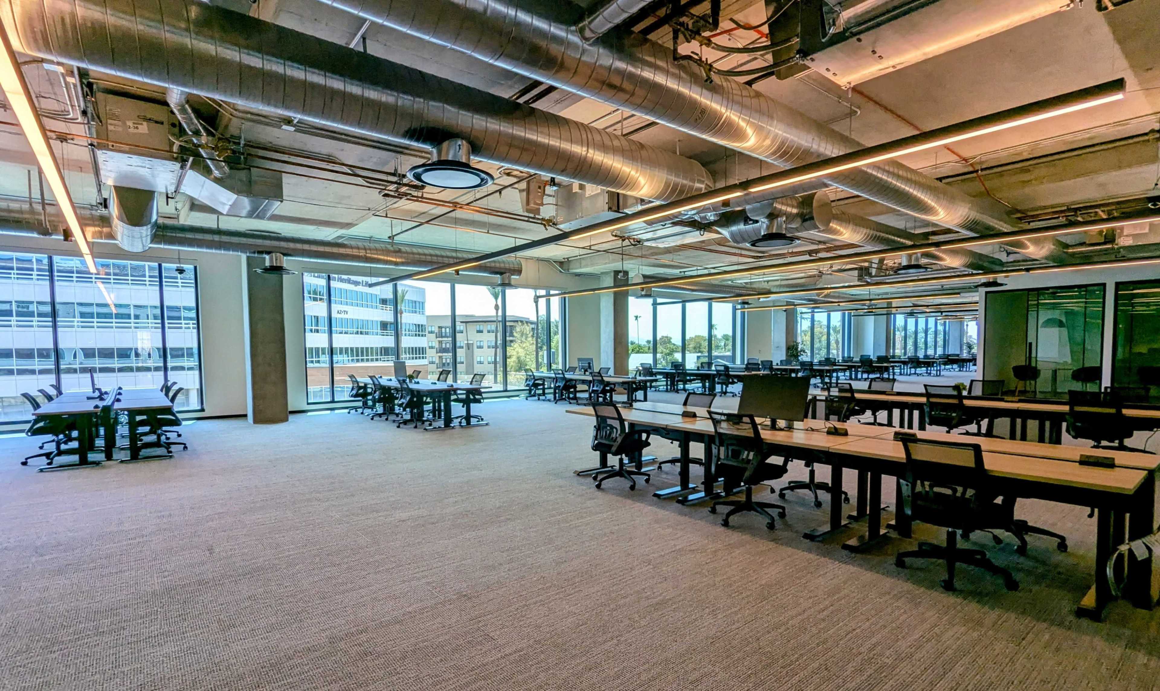 A spacious, modern office environment with multiple desks and large windows allowing natural light.