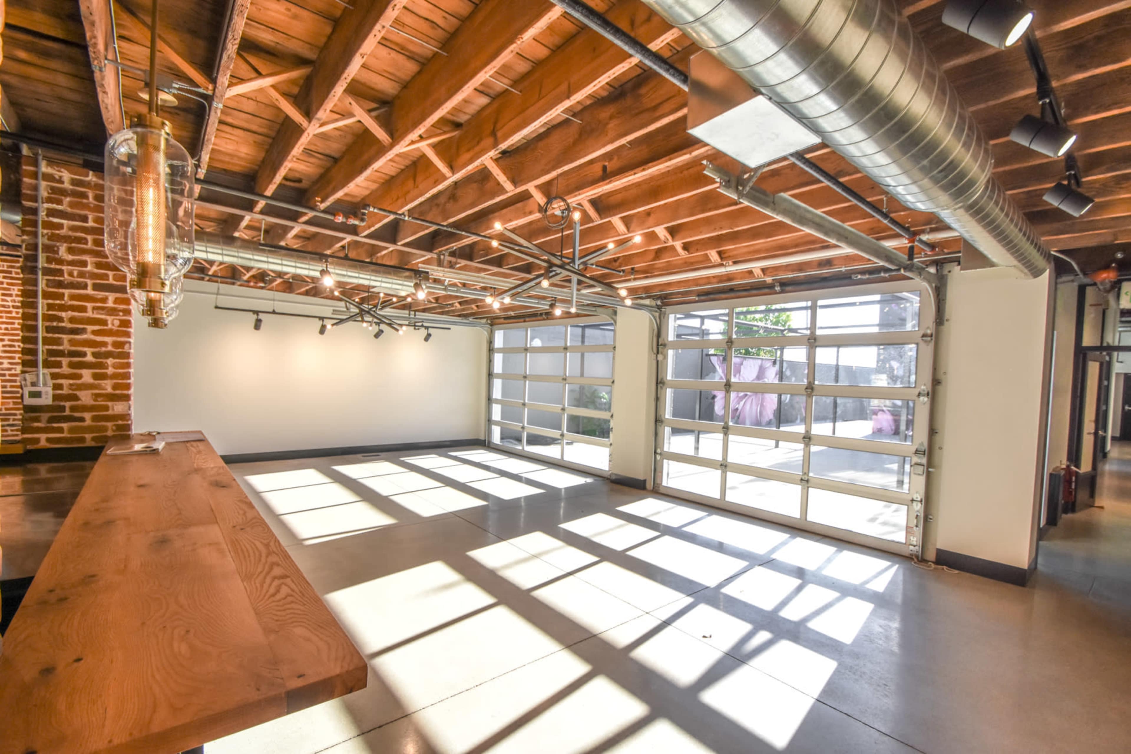 An interior space with exposed wooden beams, industrial-style lighting, and large glass doors that allow natural light to fill the area.