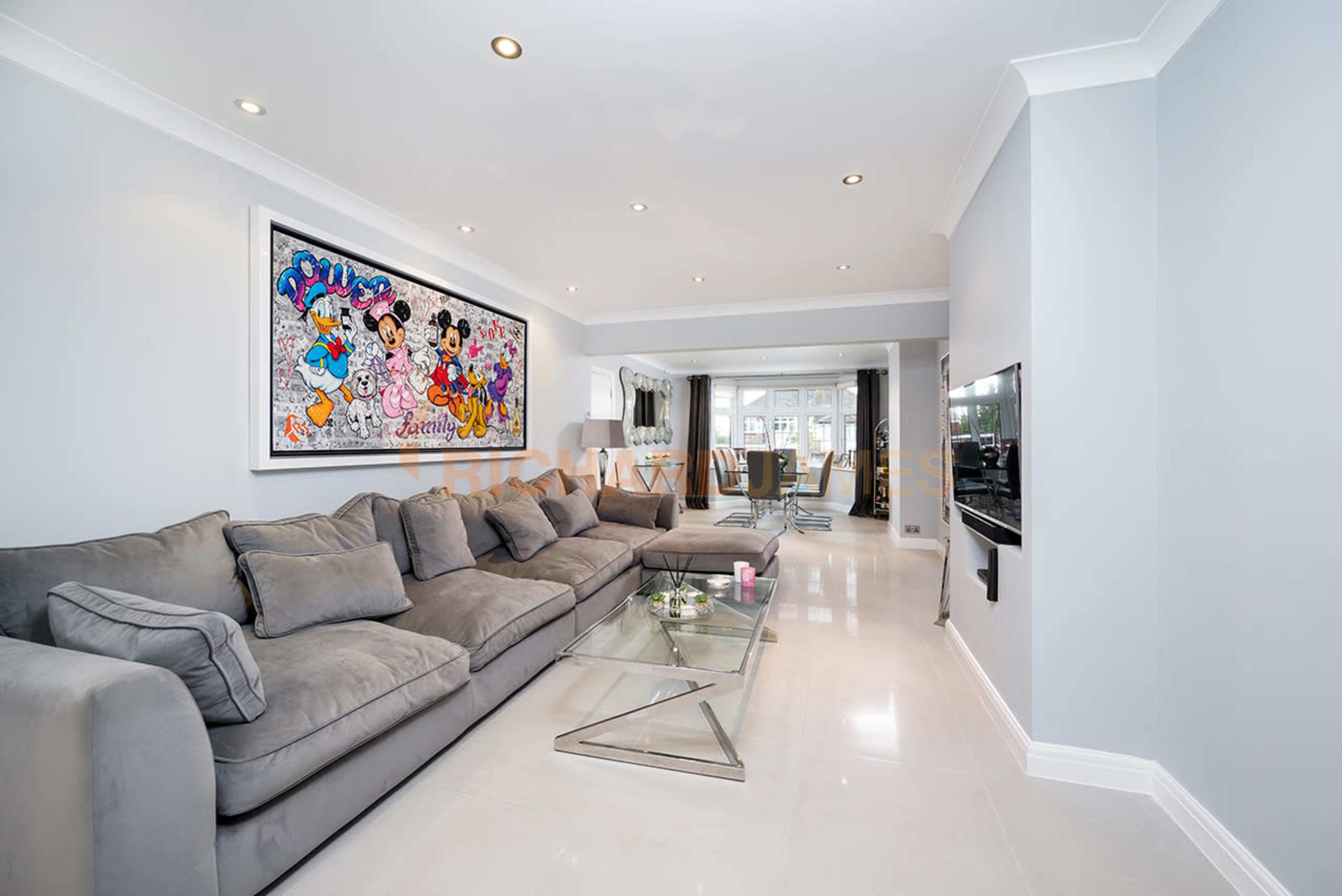 The living room features a large grey sectional sofa, a glass coffee table, and a colorful wall art piece above the couch, with sliding doors leading to an outdoor area.