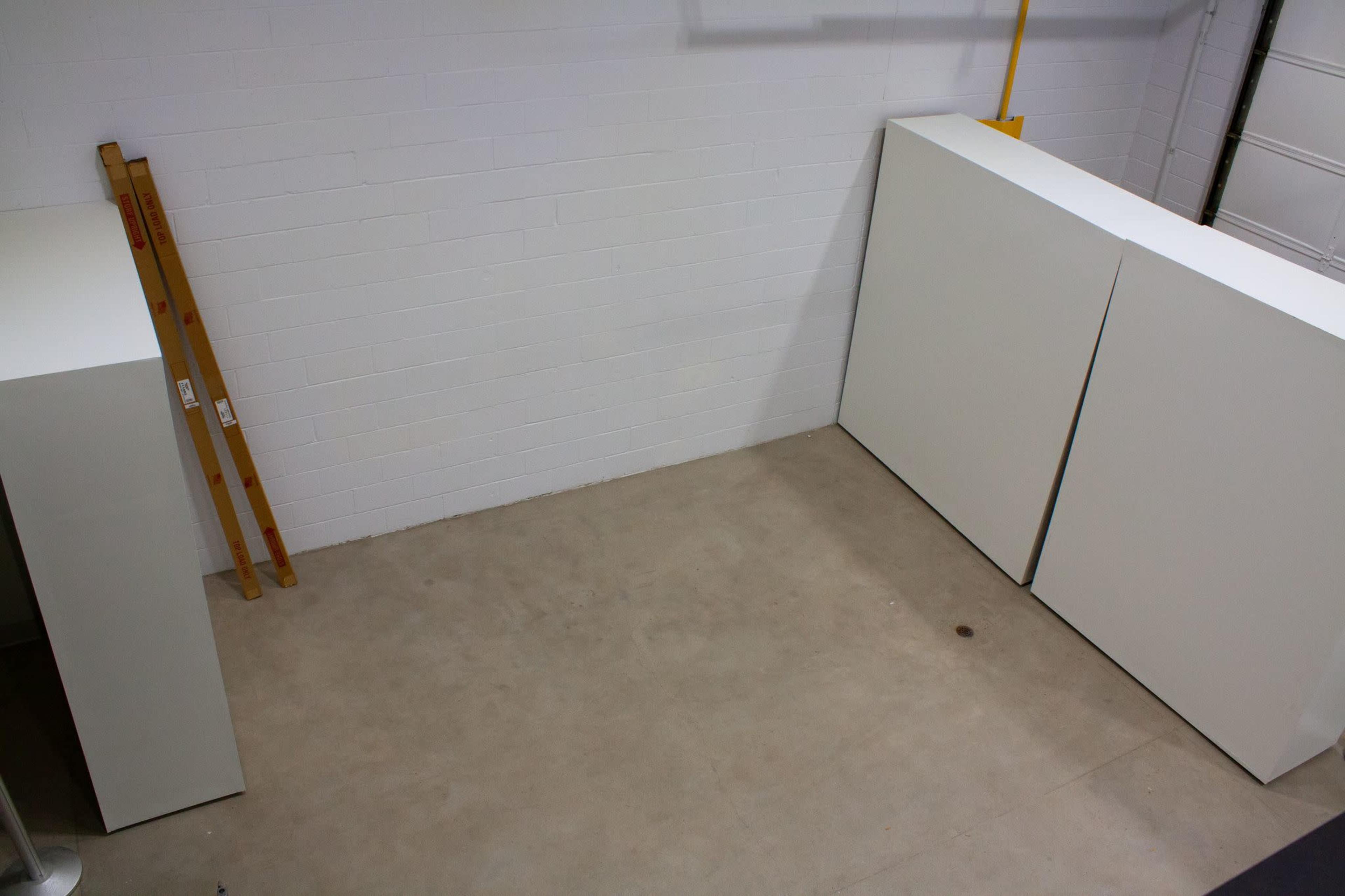 A sparse room with a concrete floor, two large white panels against the wall, and a wooden ladder leaning against the wall.