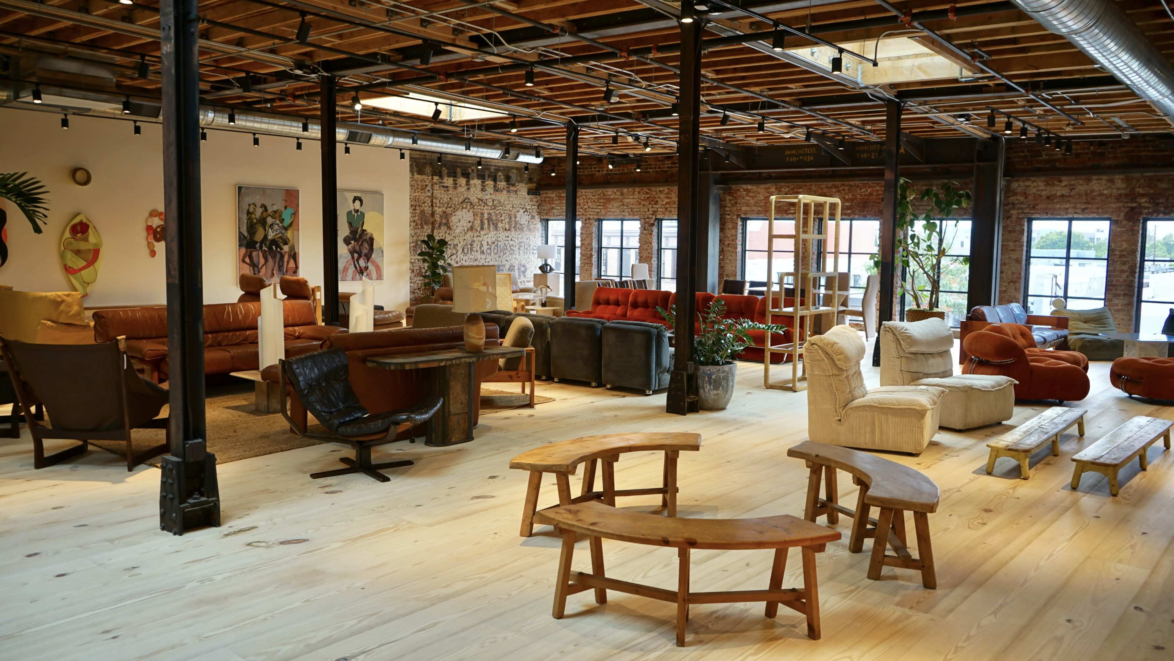 A spacious, modern lounge area with various seating options, including sofas and chairs, set against a backdrop of exposed brick walls and wooden beams.