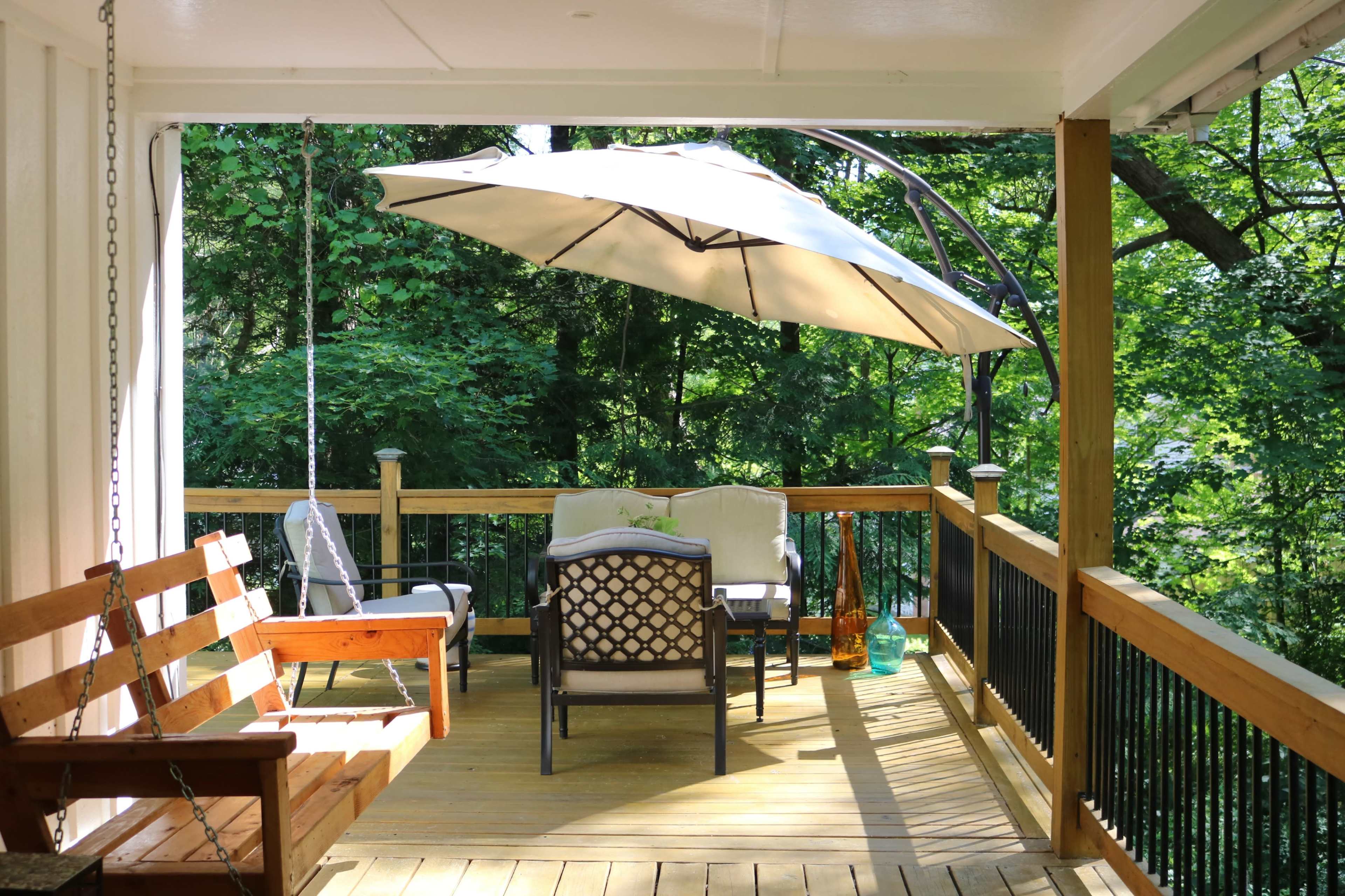 A shaded outdoor seating area features a swing and comfortable chairs surrounded by greenery.