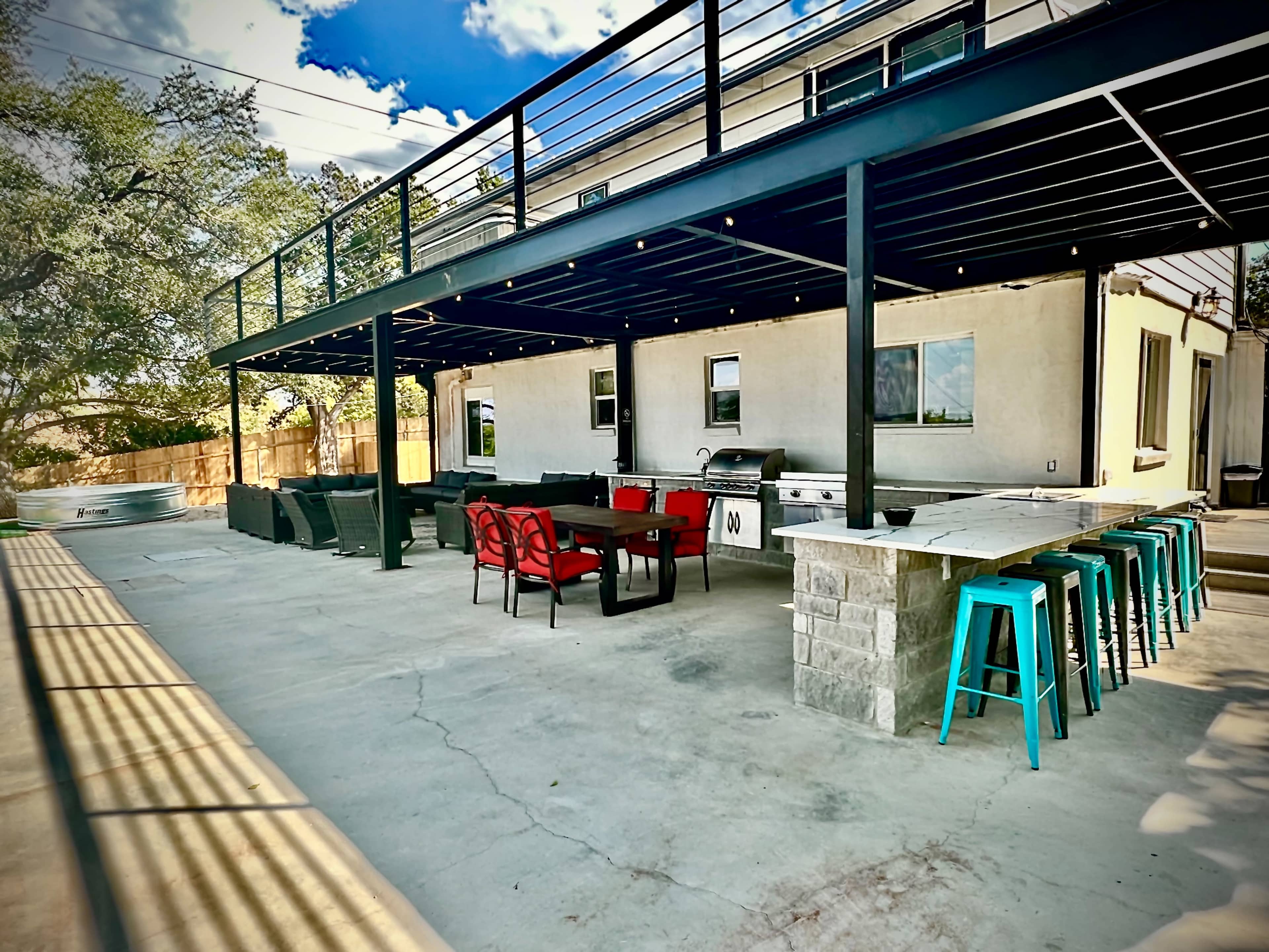 A spacious outdoor patio area with a grilling station, seating arrangements, and a covered upper deck under a clear blue sky.