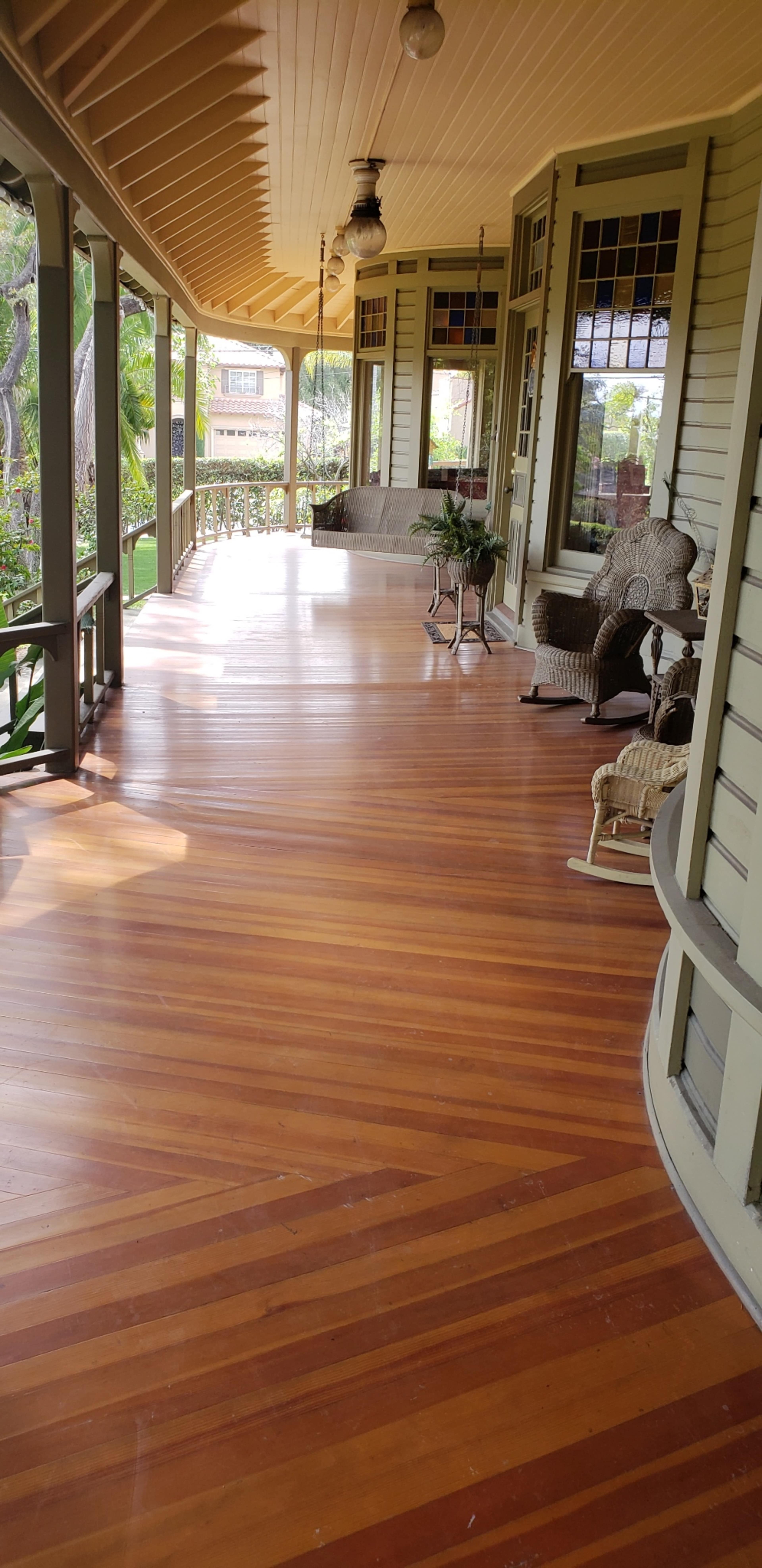 A spacious porch with polished wooden flooring and several wicker chairs arranged along the sides.