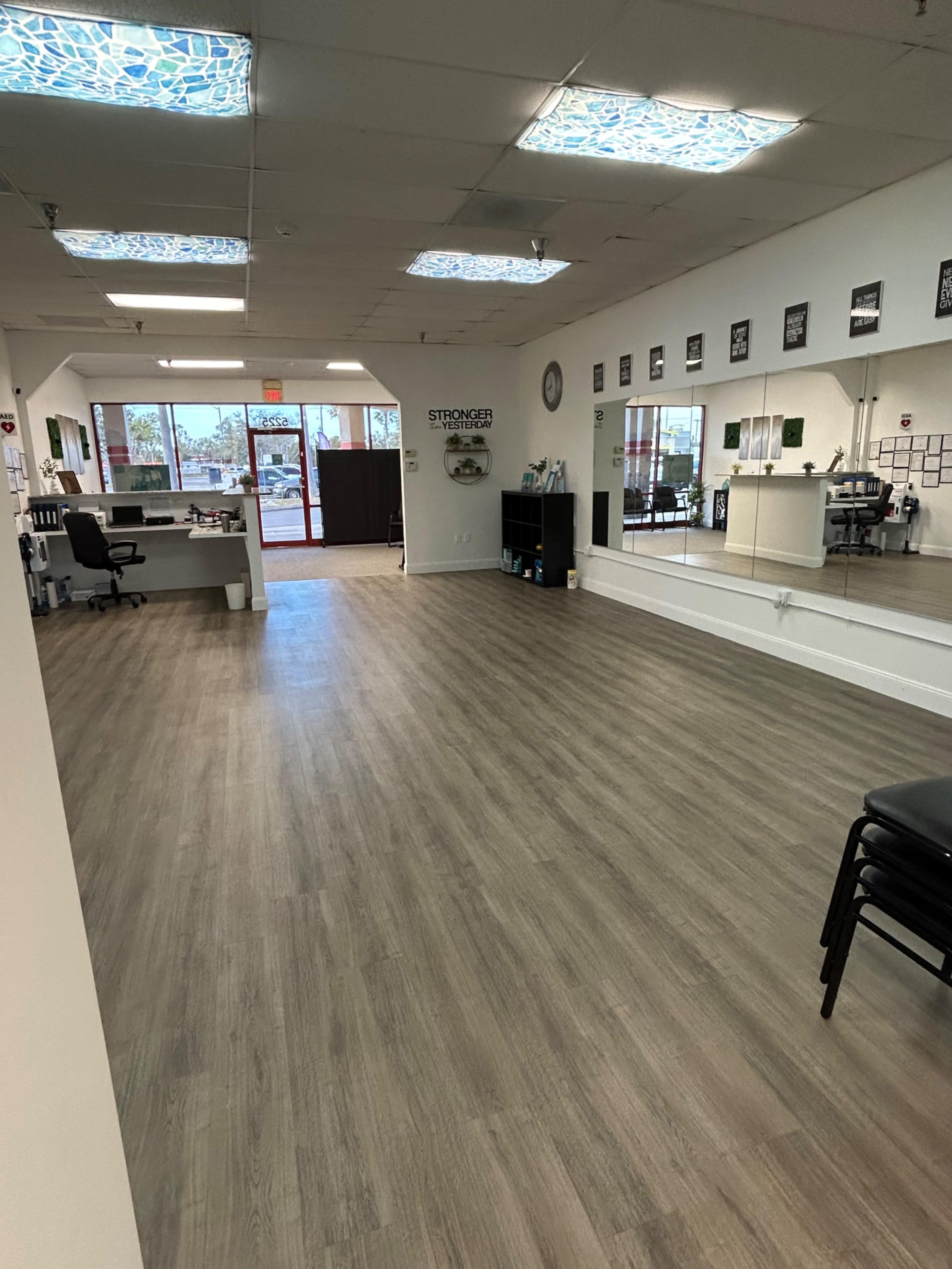 The image shows a spacious, well-lit interior of a commercial space with wooden flooring and mirrored walls.