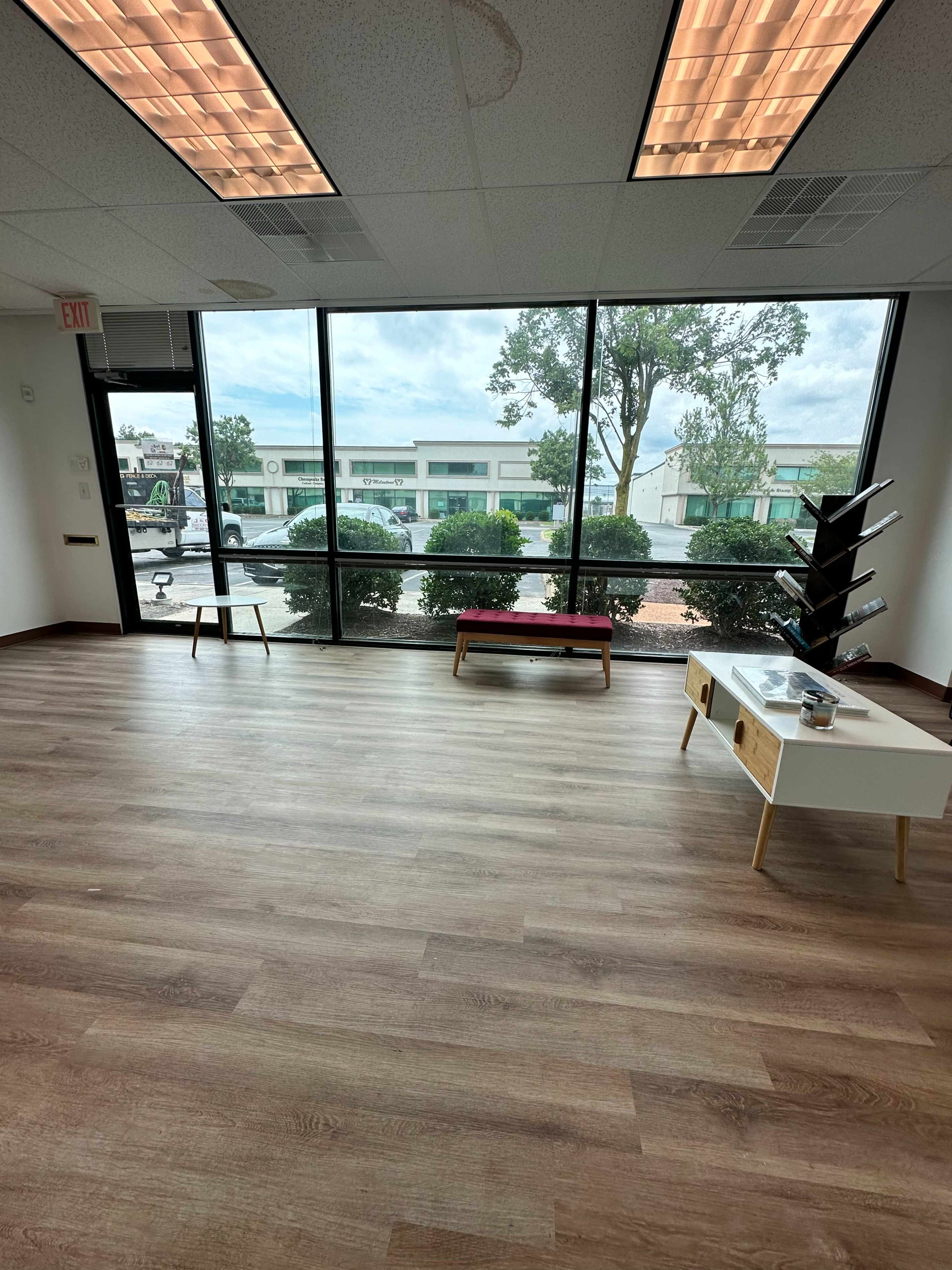 A spacious, empty interior of an office with large windows overlooking a parking lot and cloudy sky.