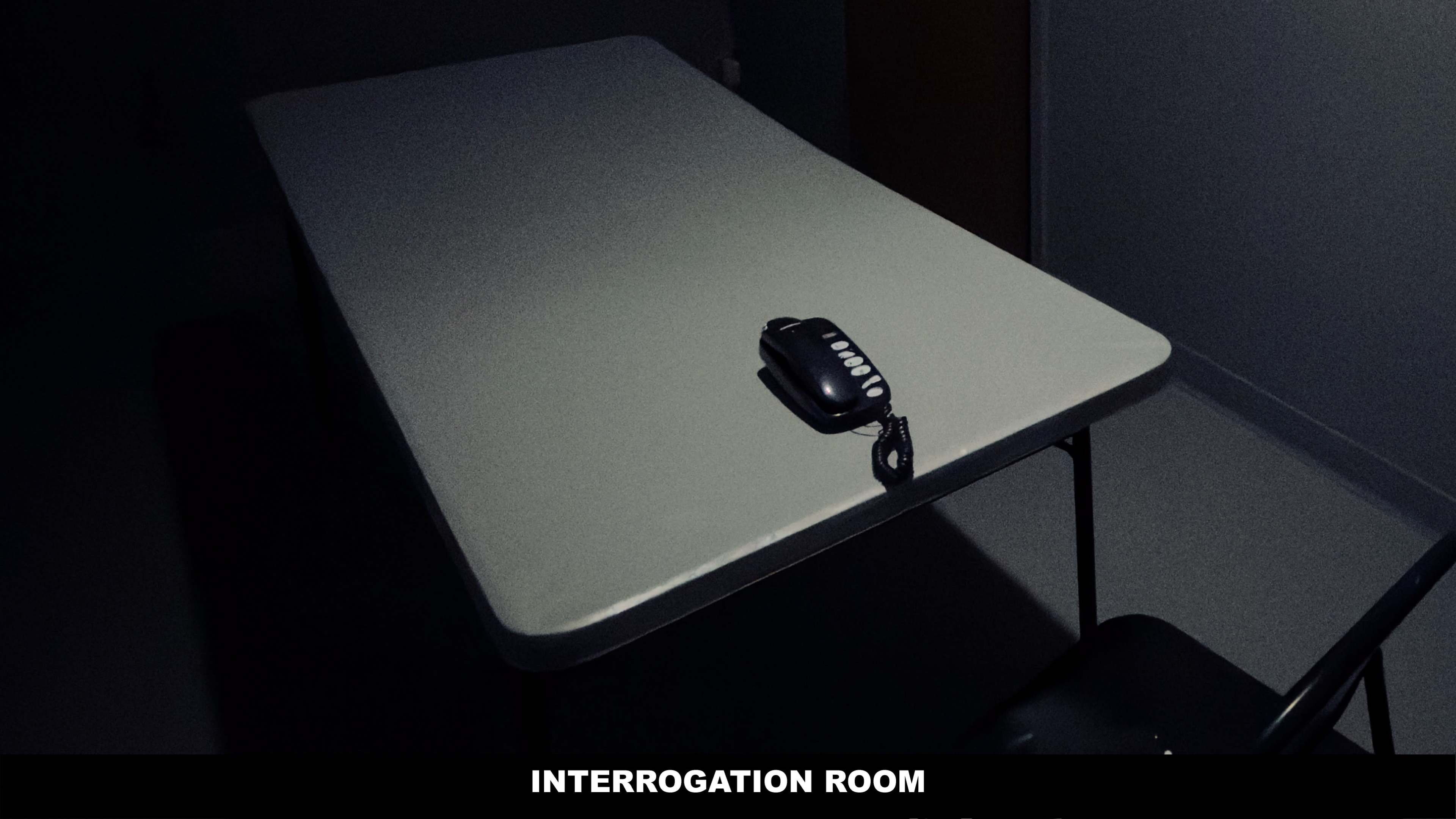 A single telephone rests on a table in a dimly lit interrogation room.