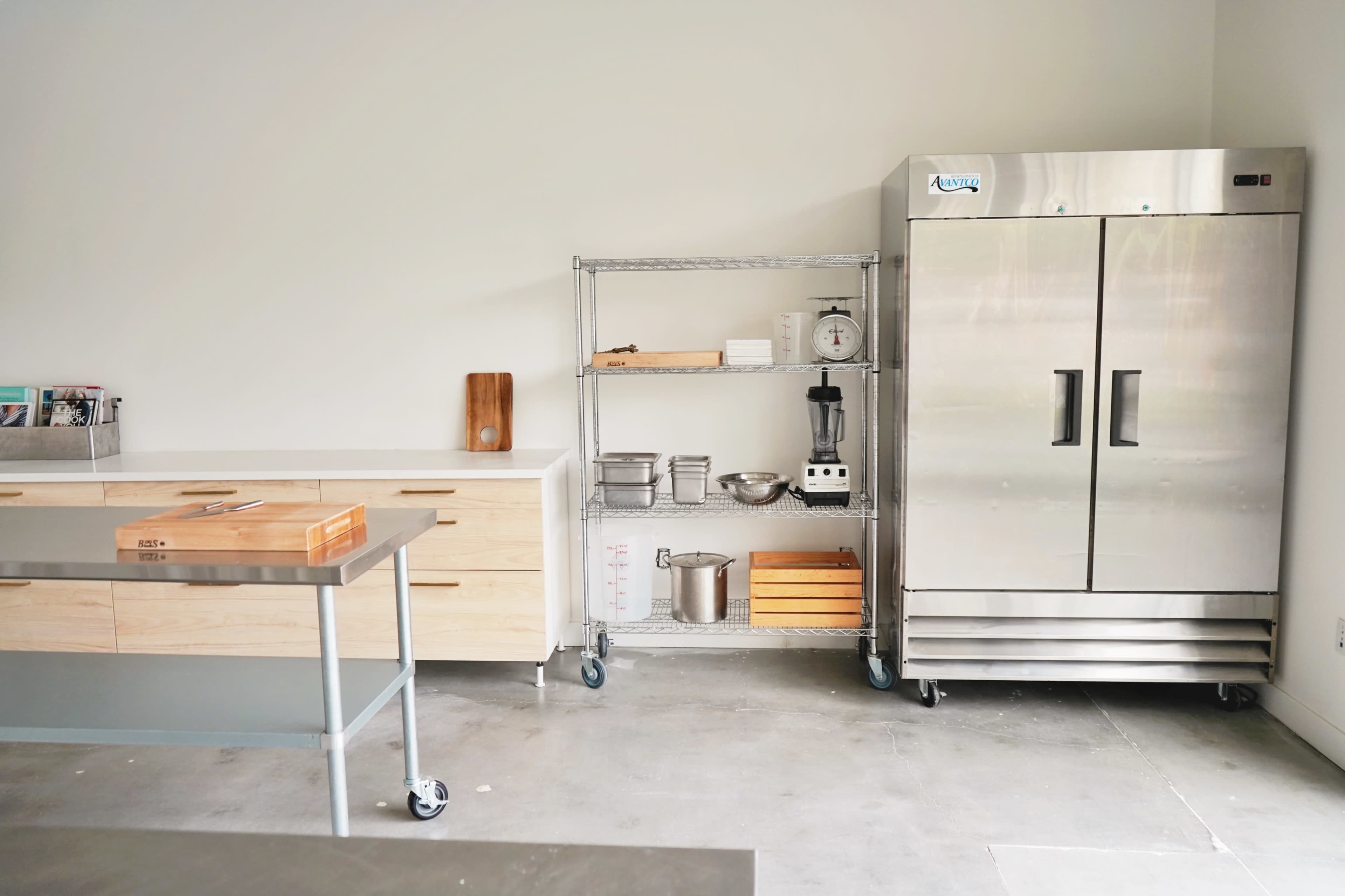 A modern kitchen with a stainless steel refrigerator, a storage cart with kitchen utensils, and a wooden countertop.