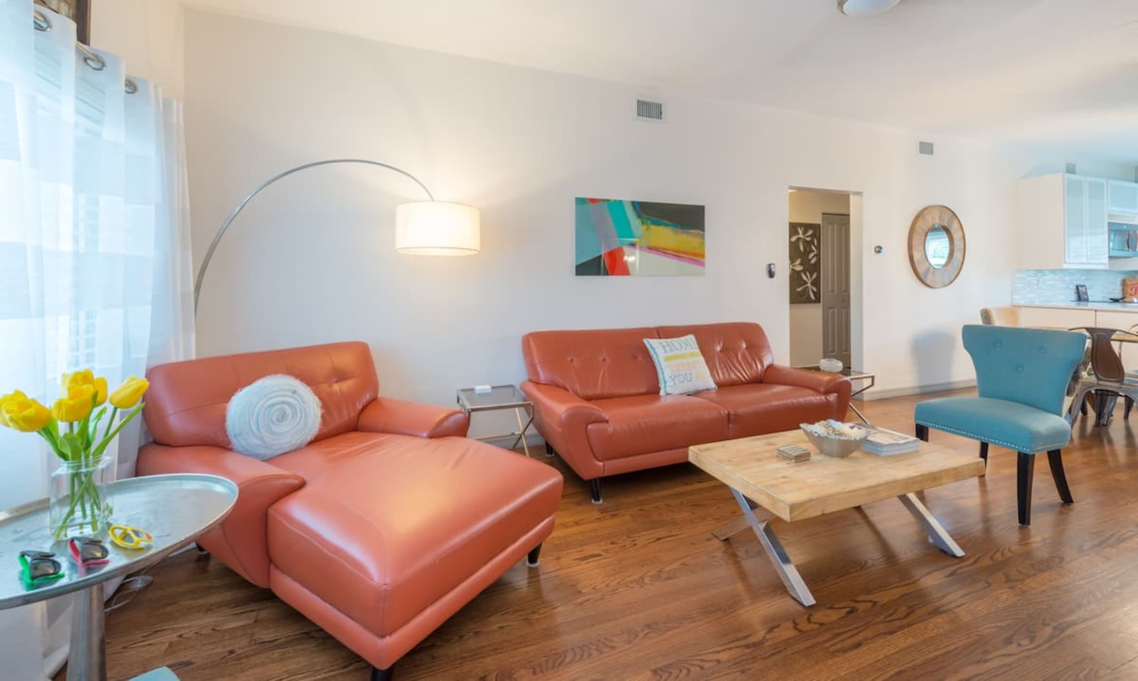 A living room with modern furniture, including two orange couches and a light wooden coffee table, set against a backdrop of white walls and hardwood flooring.