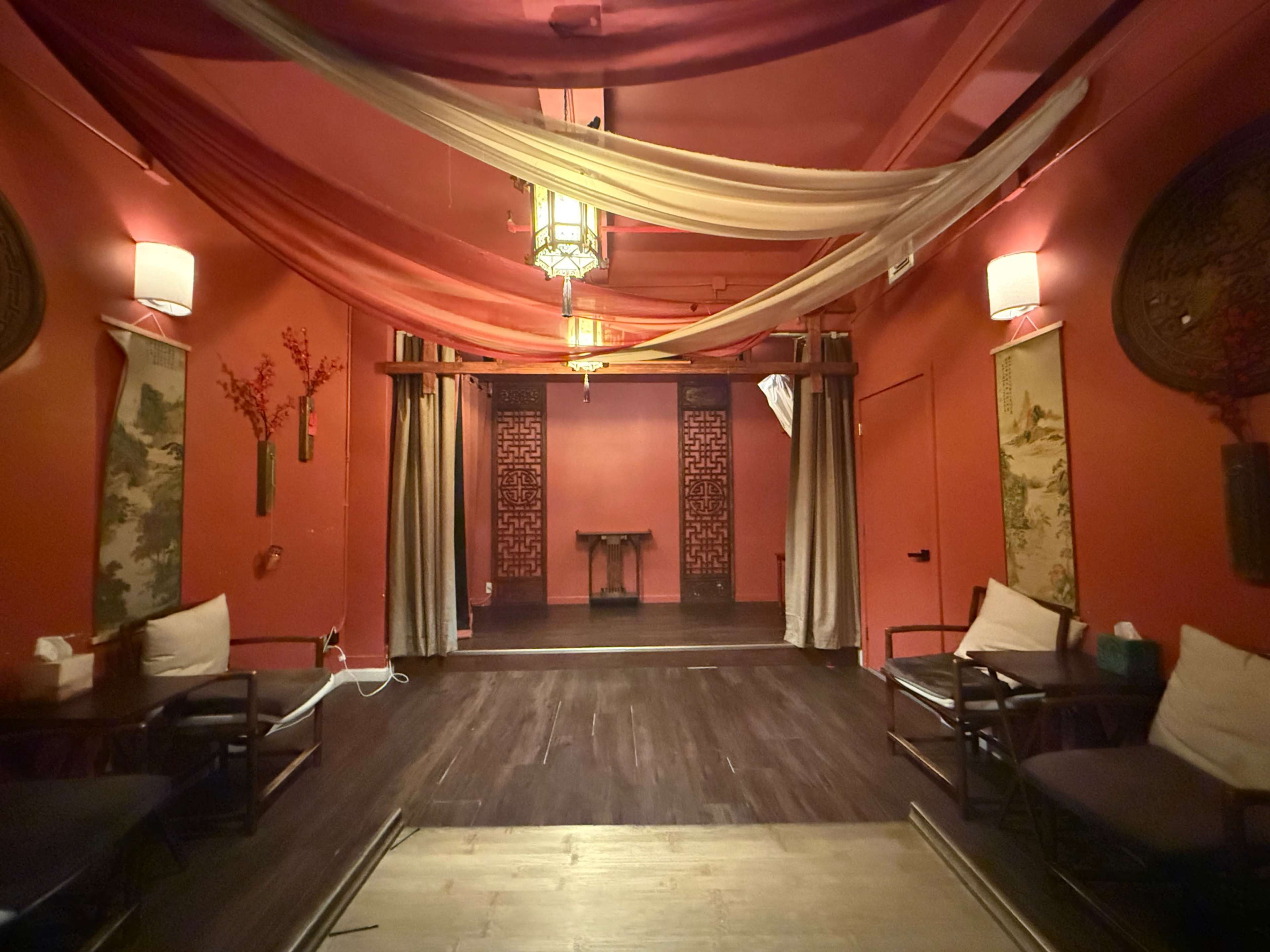 The image shows a dimly lit relaxation room with decorative drapery hanging from the ceiling, framed artwork on the walls, and seating arranged on either side.