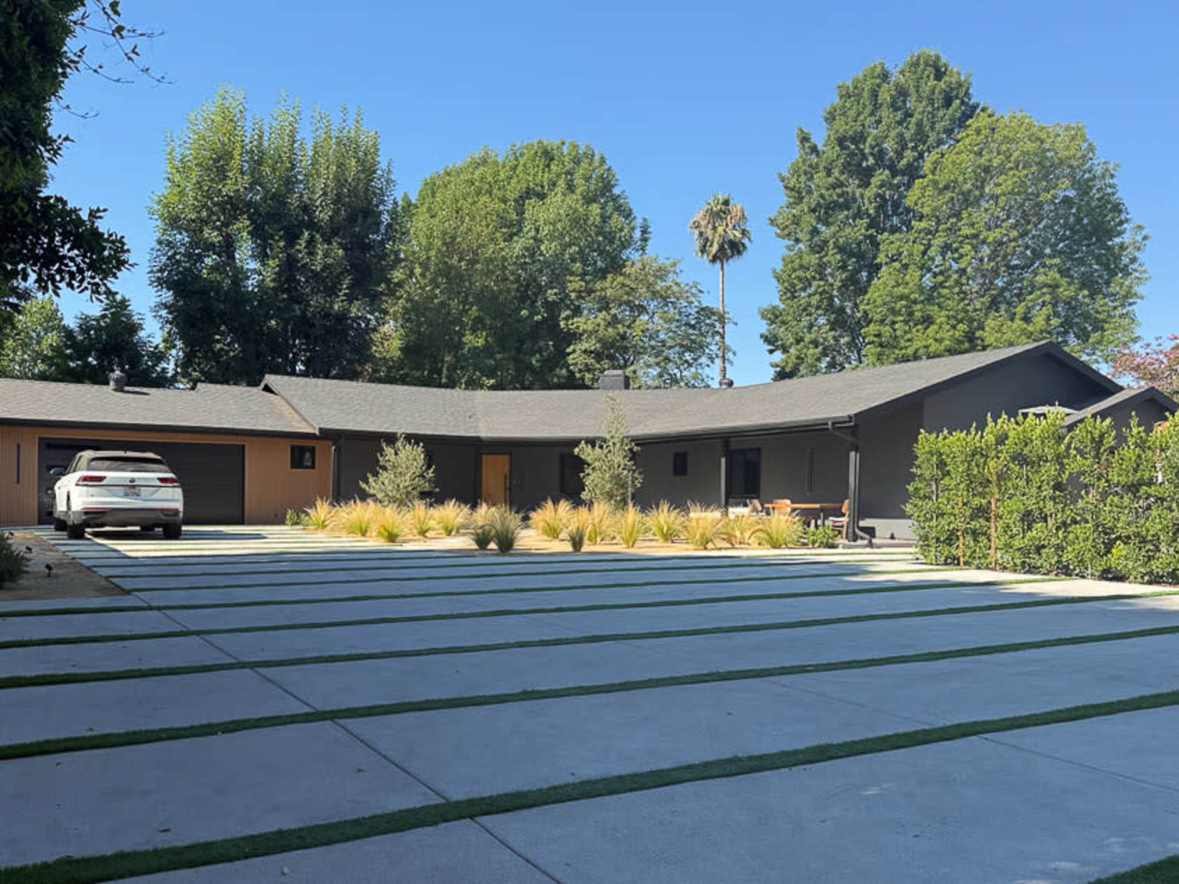 A modern single-story house is surrounded by landscaped greenery and features a driveway with alternating concrete strips and grass.