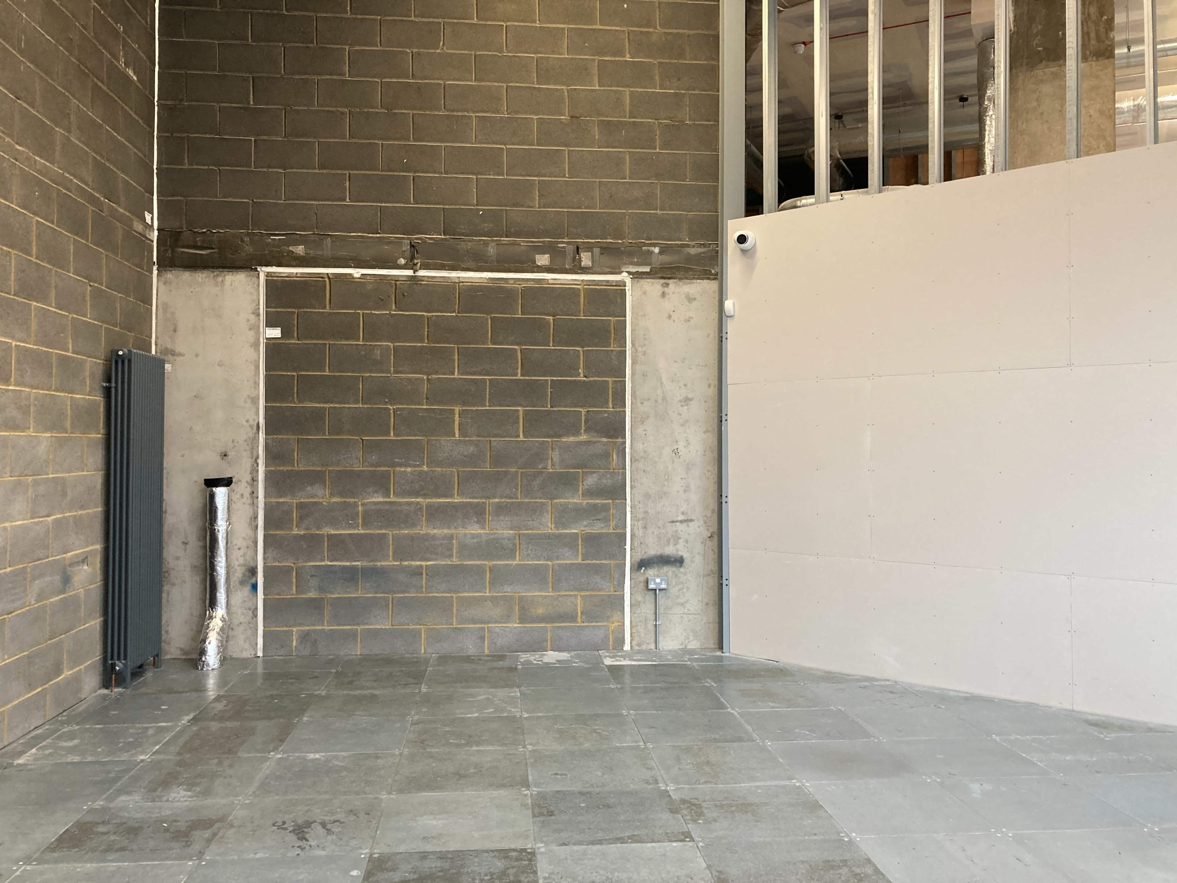 An empty interior space with exposed concrete walls, a tiled floor, and a radiator on the left side.