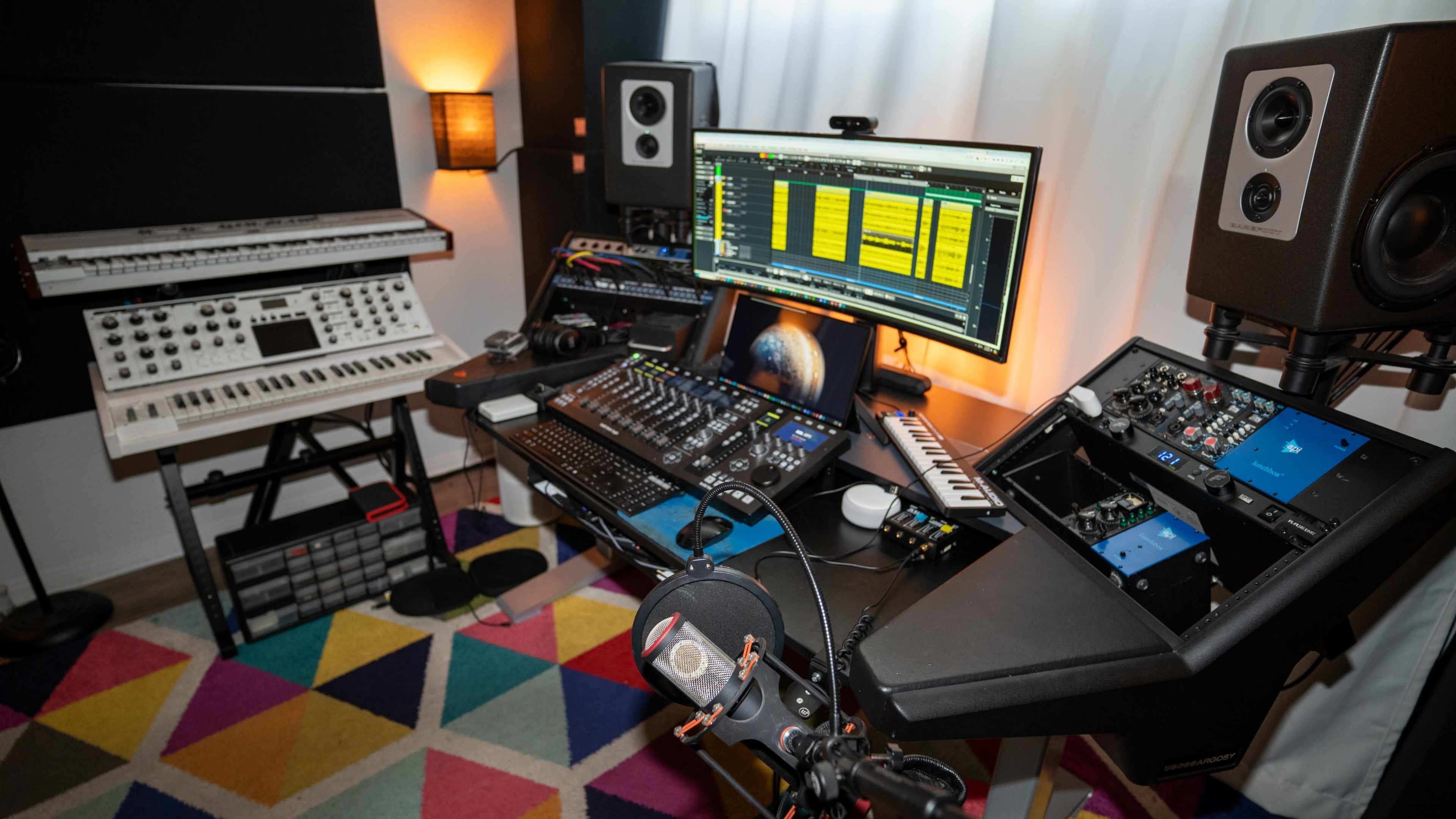 A music production studio with various synthesizers, a computer screen displaying a digital audio workstation, and professional speakers.
